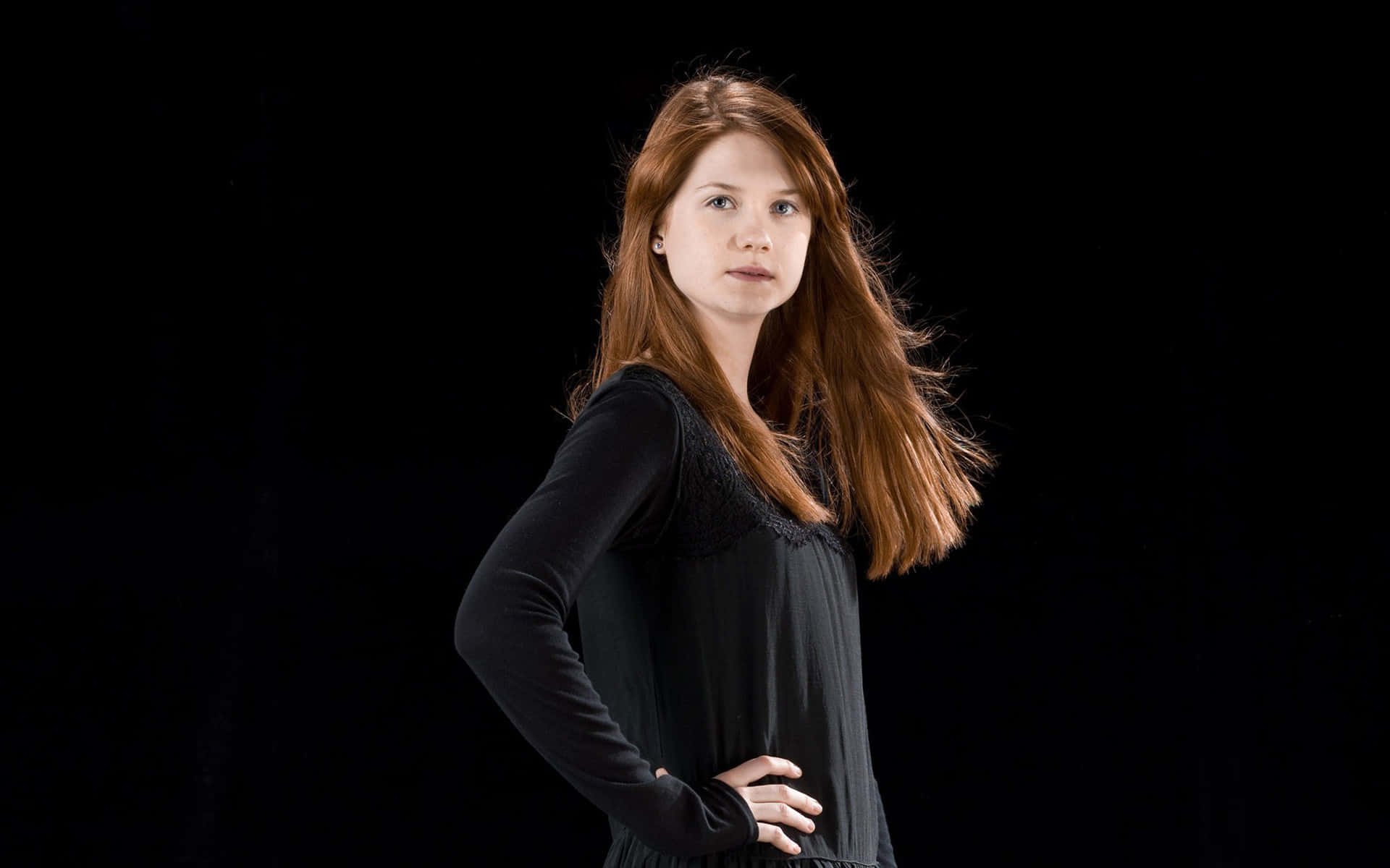 Ginny Weasley 桌布 壁紙 — 一位長紅髮的女性自信地站在黑色背景前，穿著黑色連衣裙。