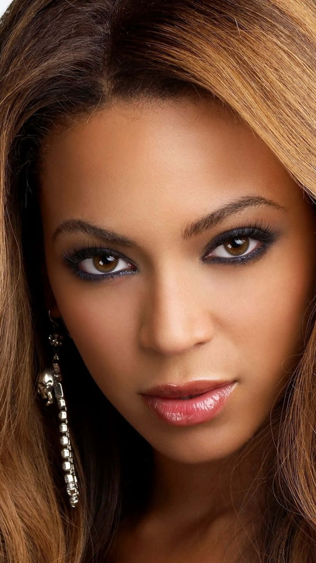 Beyoncé 桌布 壁紙 — 一位長著棕色長髮、化著引人注目的深色眼妝的女性，直視觀眾的特寫肖像。