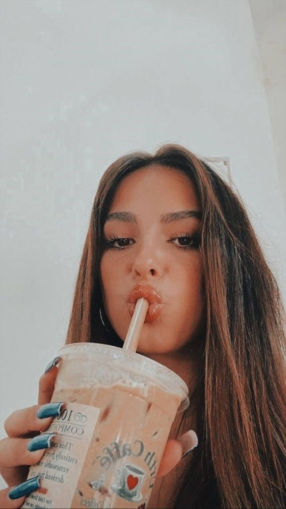 Cute Girl 桌布 壁紙 — 一位長著棕色長髮的年輕女性，用塗有青綠色指甲的手拿著杯子，透過吸管啜飲奶油冰咖啡。