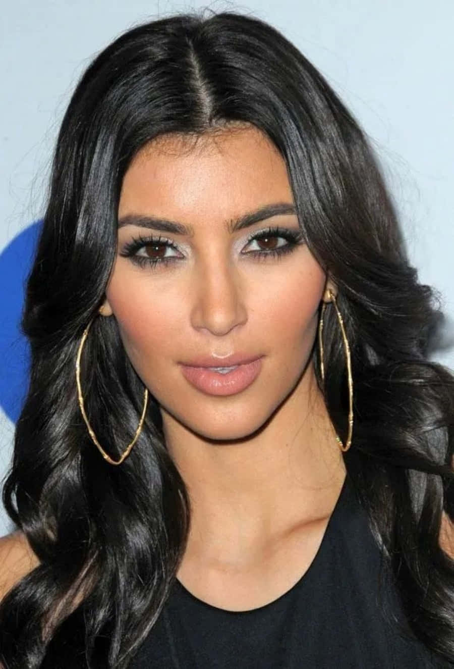 Kim Kardashian 桌布 壁紙 — 一位長著深色長波浪髮、戴著大金環耳環、身穿黑色上衣的女子的特寫肖像。