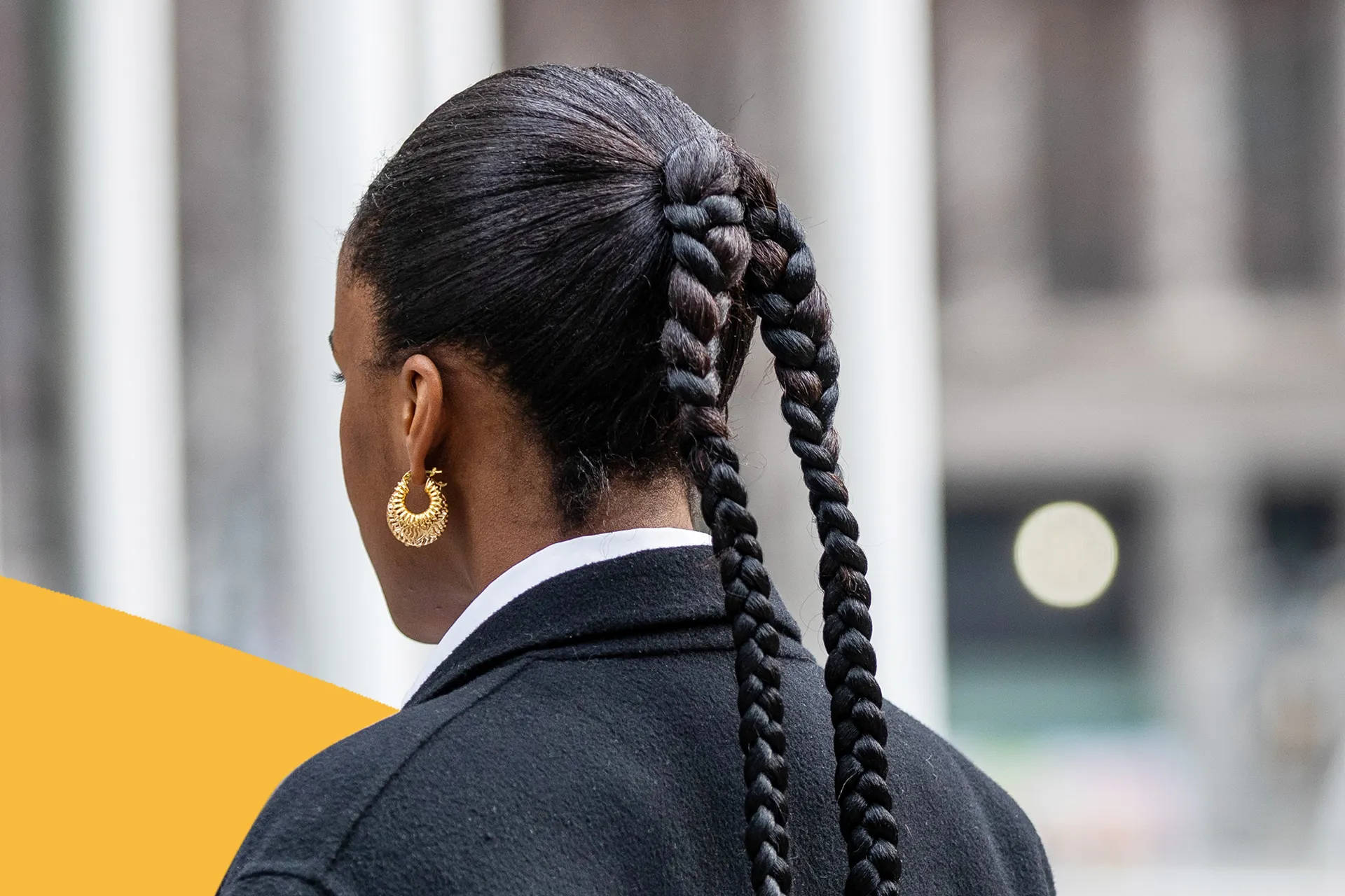 Black Woman 桌布 壁紙 — 一位長辮子頭髮、戴金色圓環耳環的女性，從背後看到穿著深色西裝外套，背景是模糊的城市景觀，帶有醒目的黃色圖形元素。
