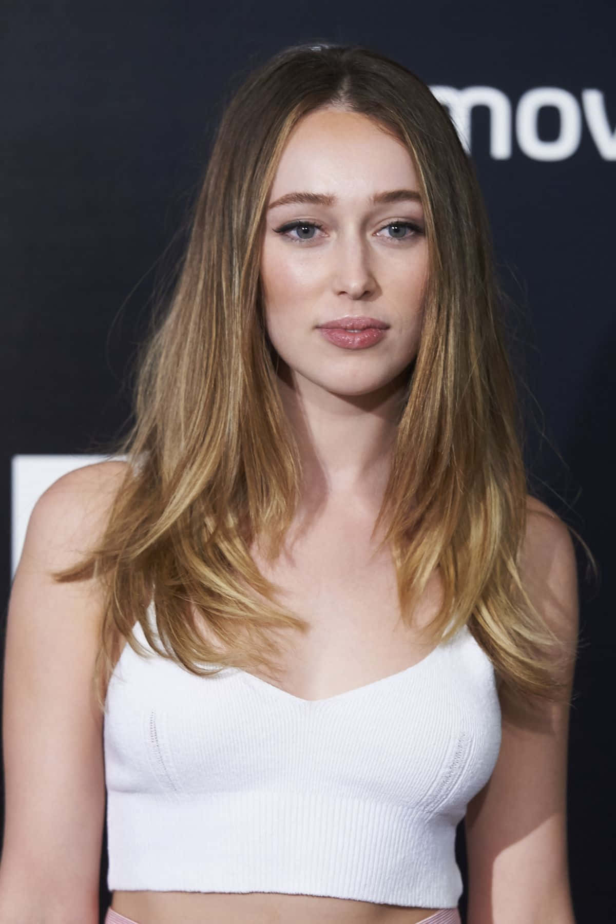 alycia debnam carey 桌布 壁紙 — 一位長金髮女性穿著白色羅紋短上衣，在帶有部分白色文字的深色背景前擺姿勢。