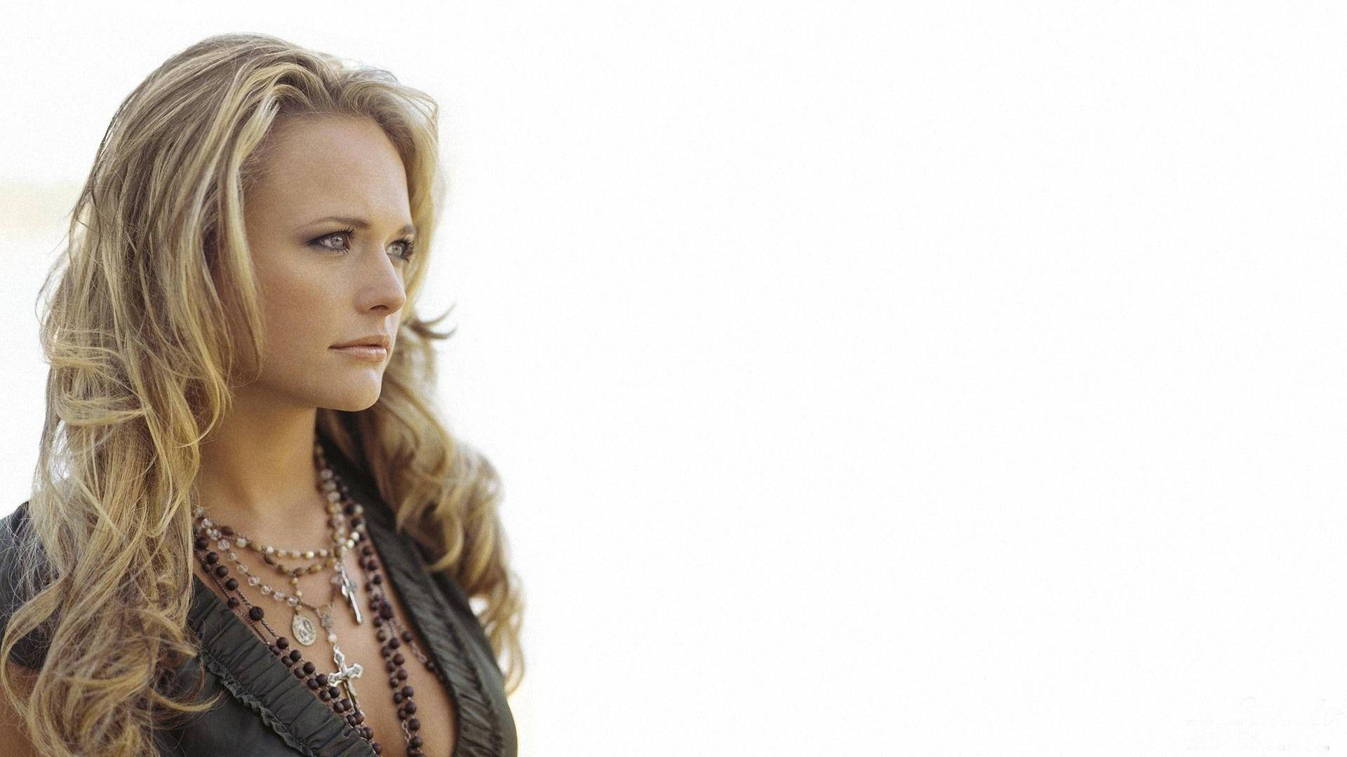 Miranda Lambert 桌布 壁紙 — 一位長金髮的女性在明亮的白色背景下戴著層疊項鍊，若有所思地凝視著。