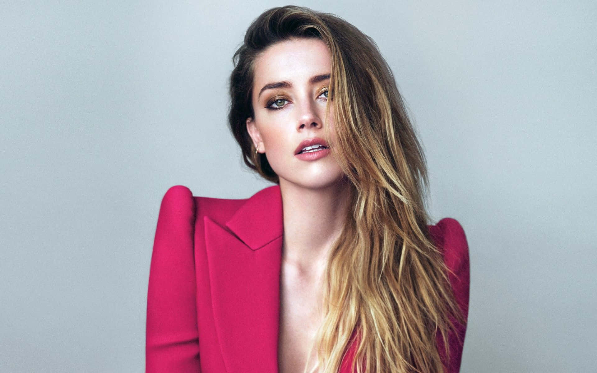Amber Heard 桌布 壁紙 — 一位長金髮的女性在柔和的灰色工作室背景前穿著大膽的粉紅色西裝外套。