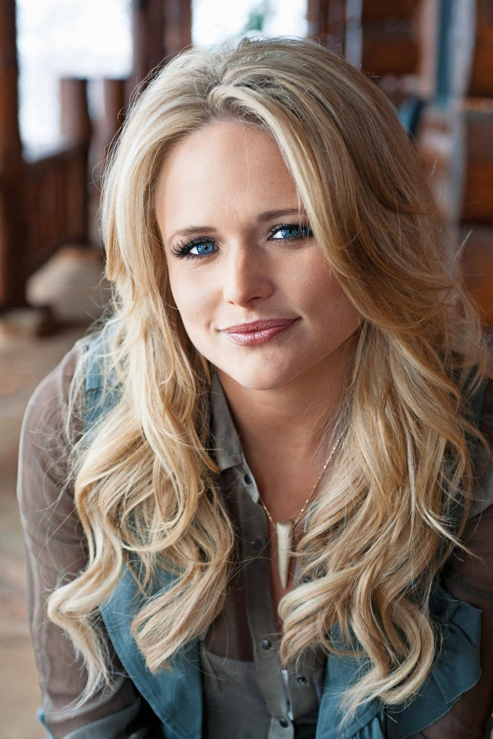 Miranda Lambert 桌布 壁紙 — 一位長金髮藍眼睛的女性在室內穿著牛仔背心，溫柔地微笑。