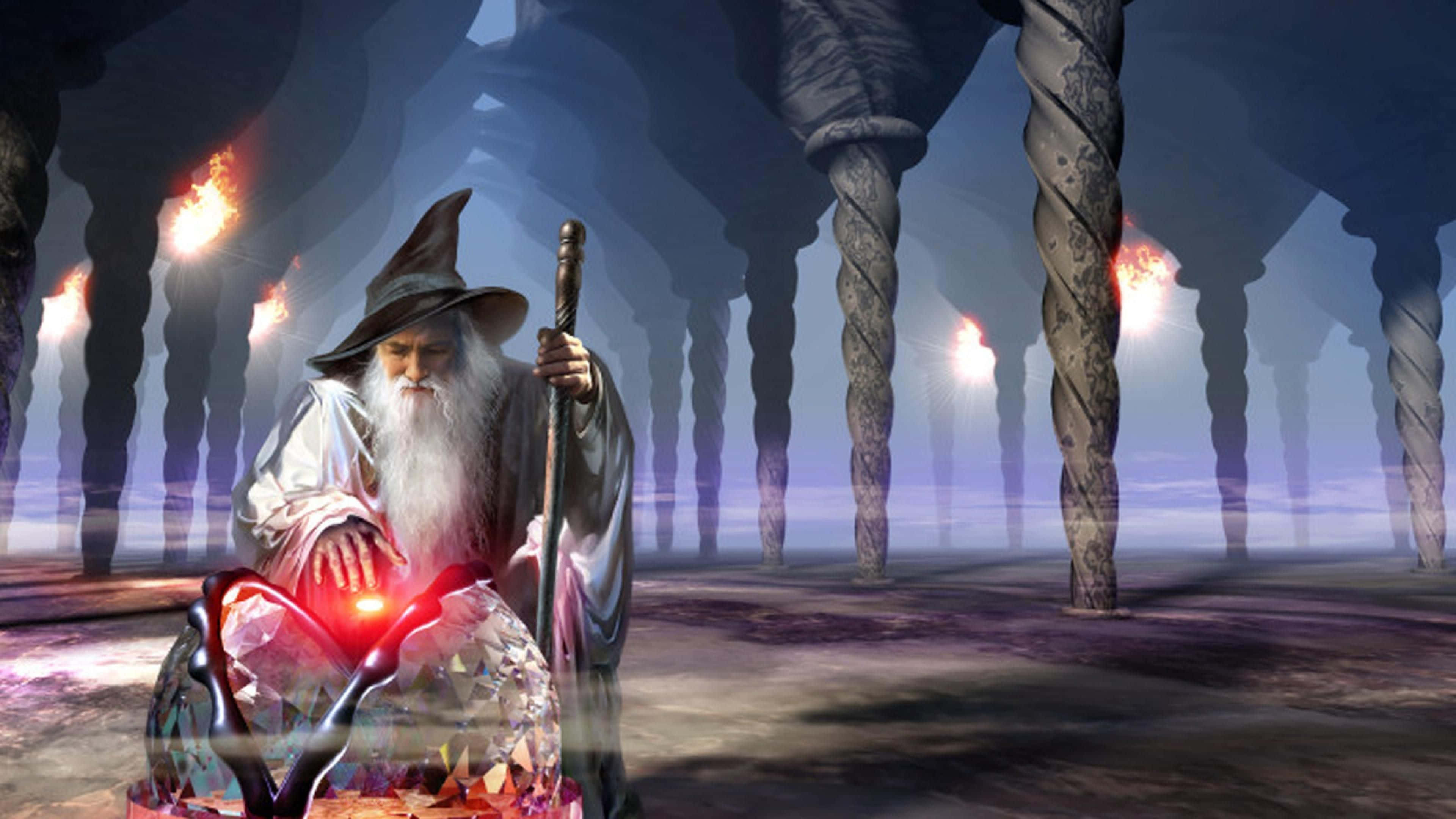 Wizardry 桌布 壁紙 — 一位長長白鬍鬚、戴尖帽的老巫師，在一個由扭曲柱子上火炬照亮的奇幻洞穴中，手持一顆發光的紅色水晶球。