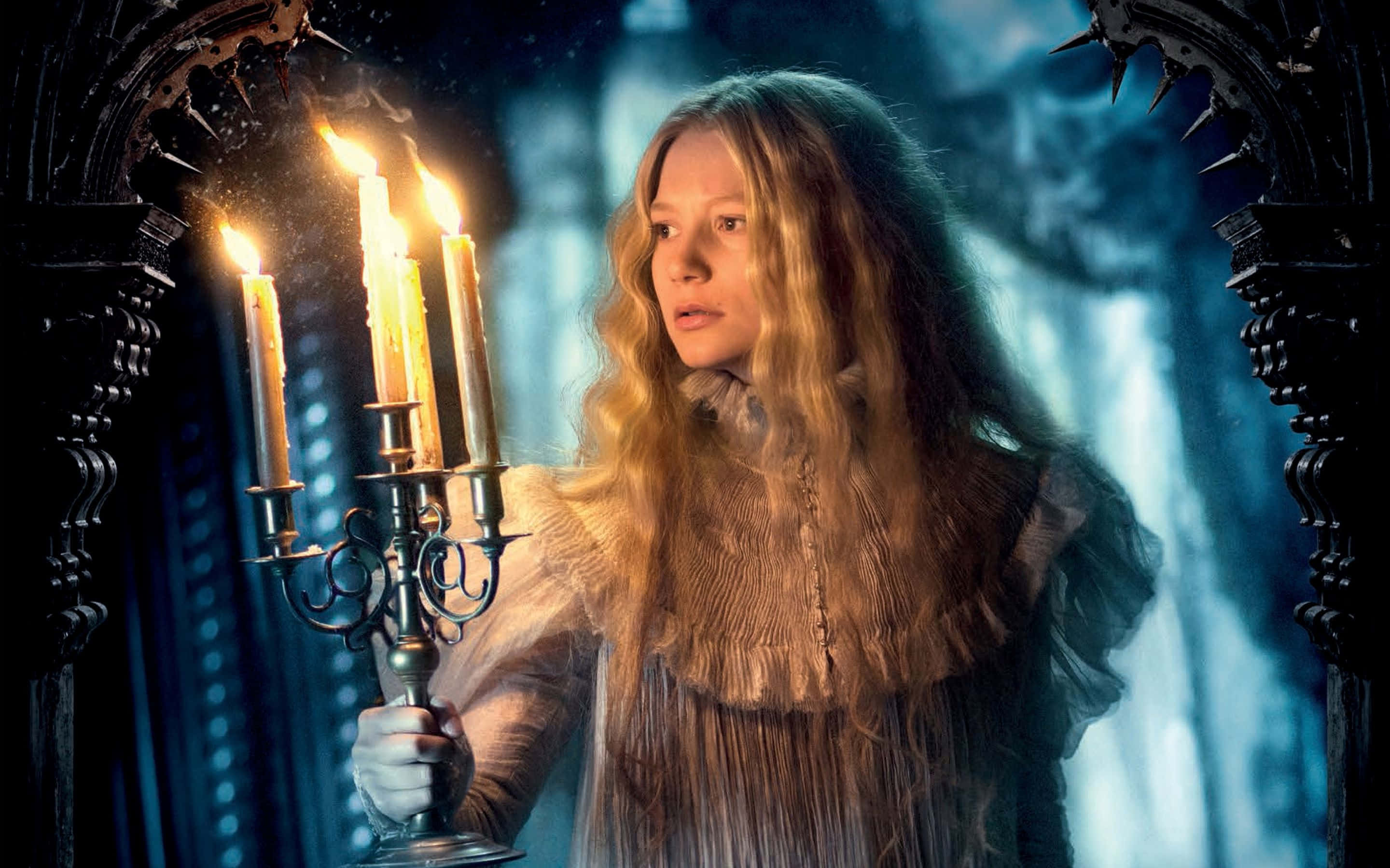 Mia Wasikowska 桌布 壁紙 — 一位長長金髮的年輕女性在黑暗的哥德式拱門中手持點燃的燭台，溫暖的光芒映照在冰冷的藍色背景上。