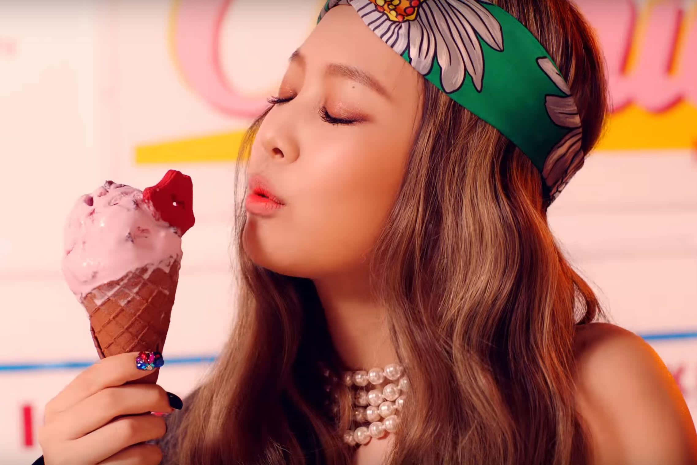 Jennie Kim 桌布 壁紙 — 一位長髮戴花頭帶的年輕女性閉上眼睛享受草莓冰淇淋甜筒。