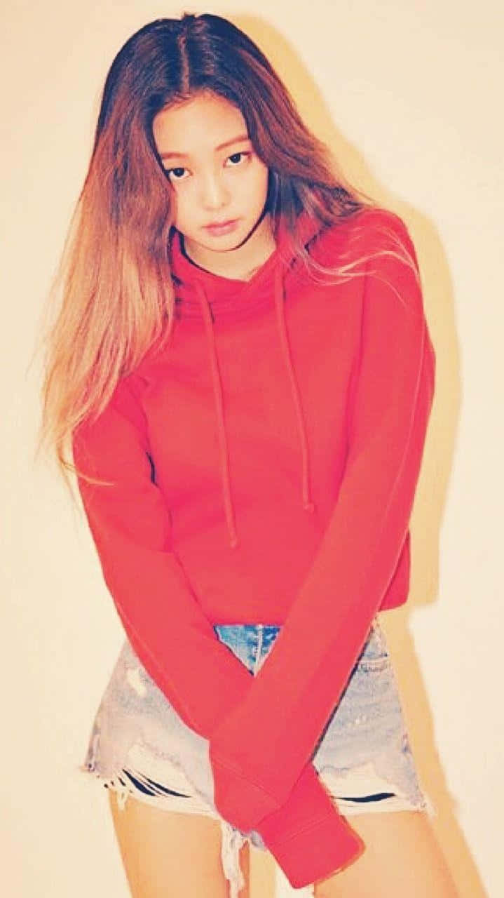 Jennie Kim 桌布 壁紙 — 一位長髮漸層染色的年輕女性，在純色溫暖背景前穿著鮮紅色連帽衫和破損牛仔短褲。