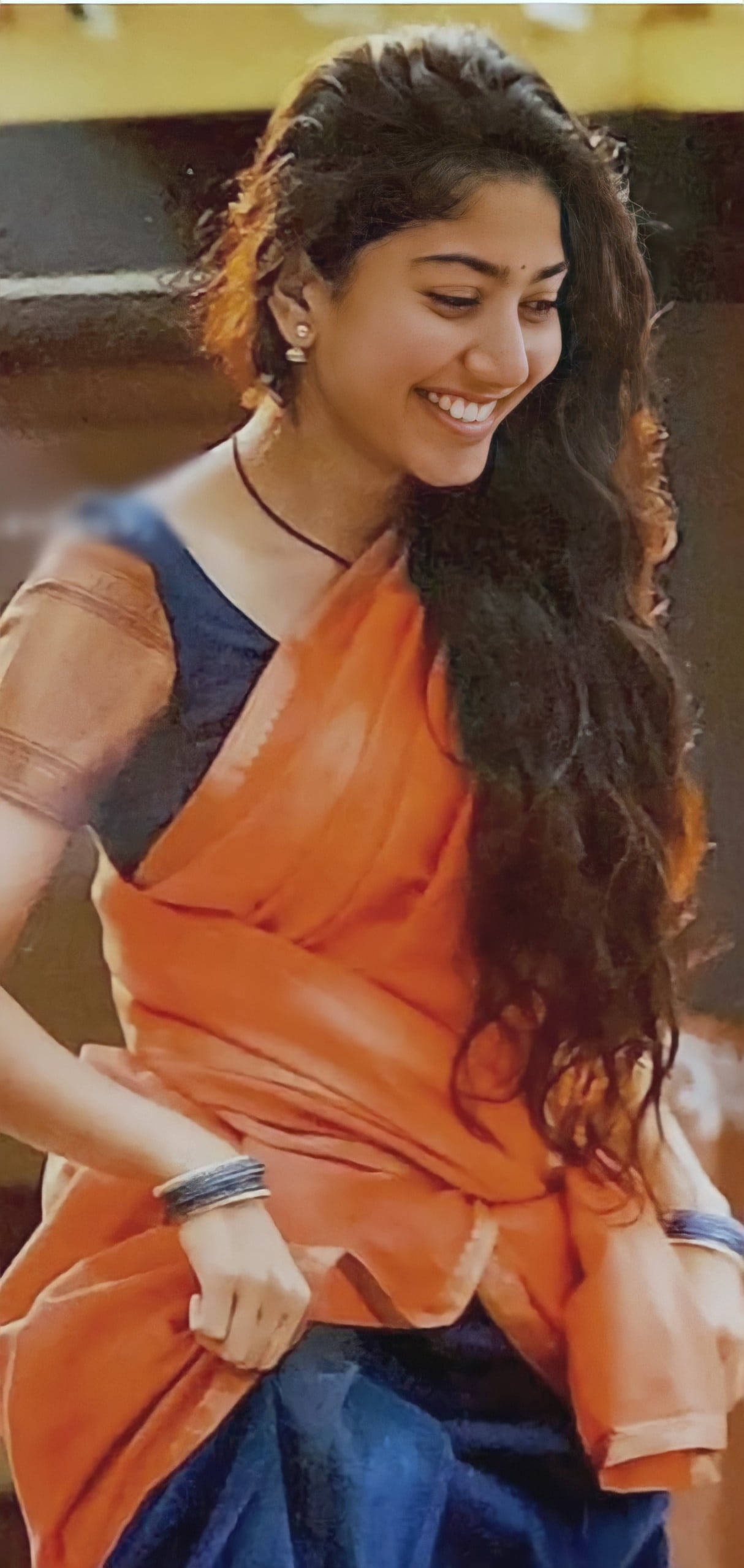 smiling 桌布 壁紙 — 一位長黑髮的女性戴著傳統珠寶，穿著鮮豔的橙色和藍色紗麗，溫暖地微笑。