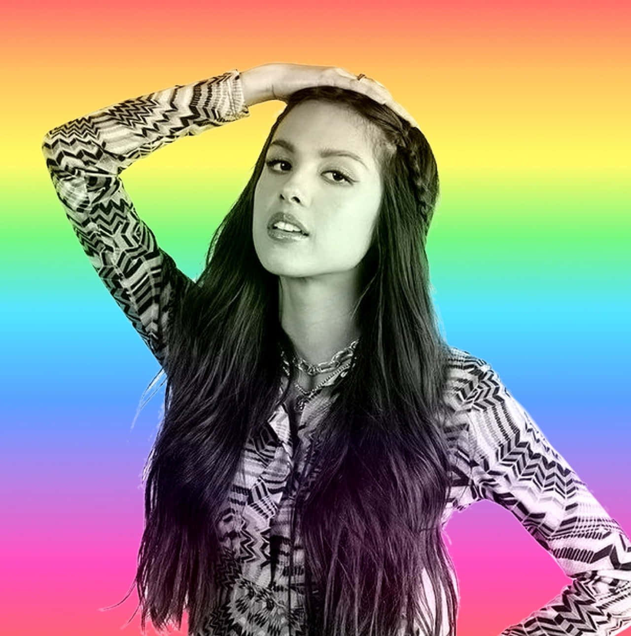 Olivia Rodrigo 桌布 壁紙 — 一位長黑髮的年輕女性在鮮豔的彩虹漸變背景前自信地擺姿勢。