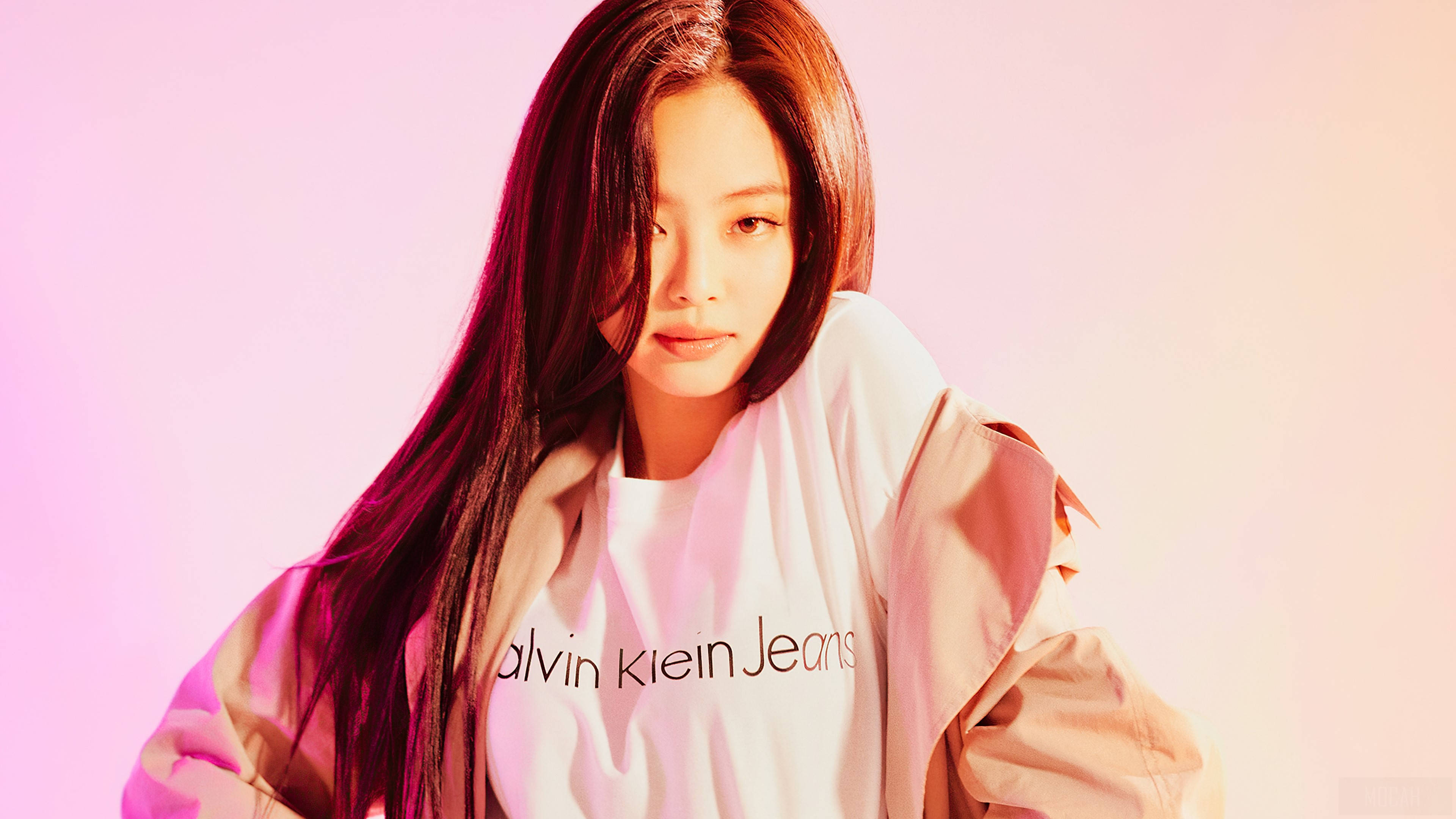 BLACKPINK Jennie Calvin Klein 壁紙 — 一位長黑髮的年輕女性穿著白色Calvin Klein Jeans襯衫和米色外套，背景是柔和的粉紅和蜜桃漸變色。