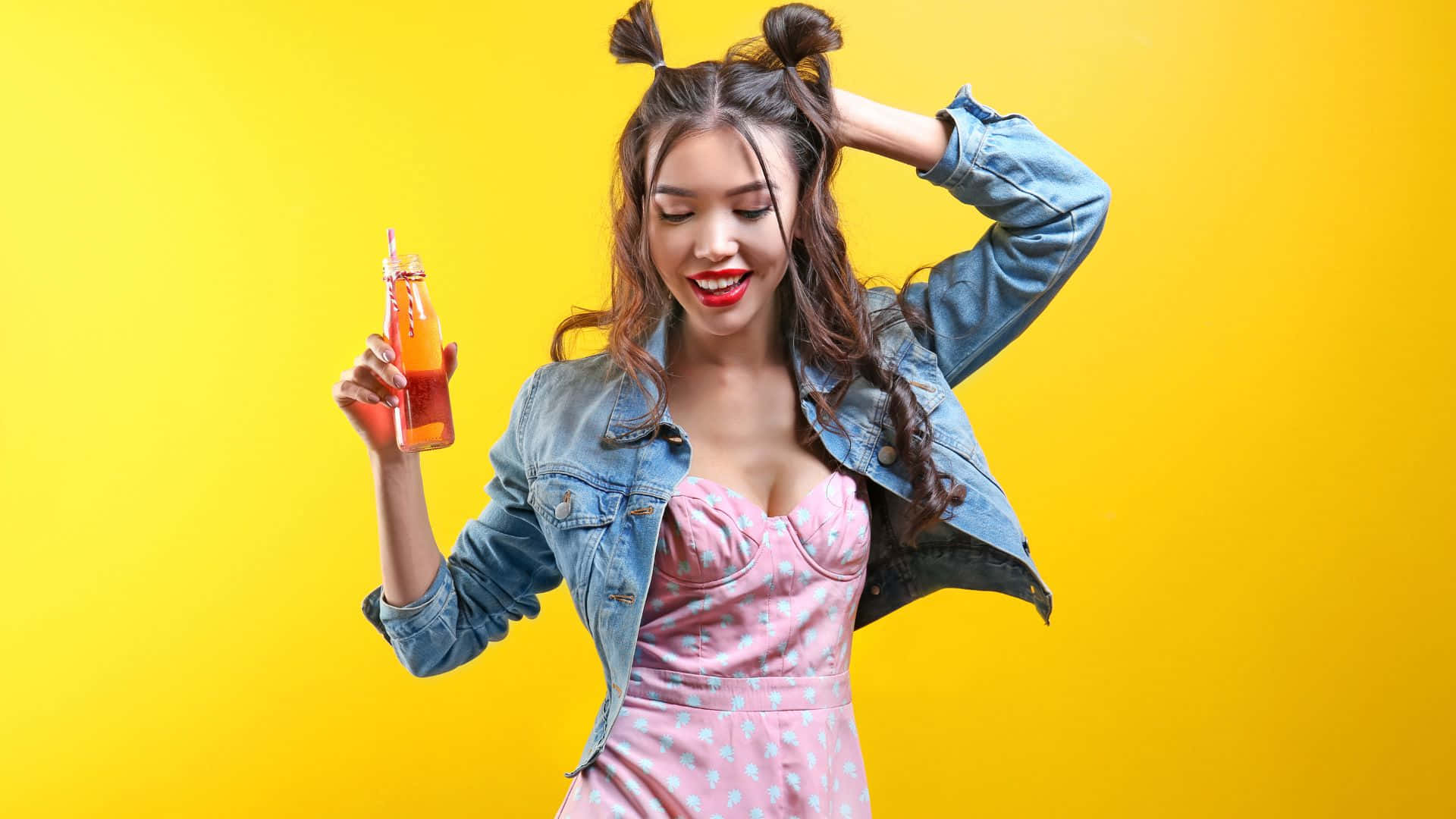 Hipster 桌布 壁紙 — 一位開心的年輕女性紮著雙丸子頭，在明亮的黃色背景前微笑著手持一瓶橙汁玻璃瓶。