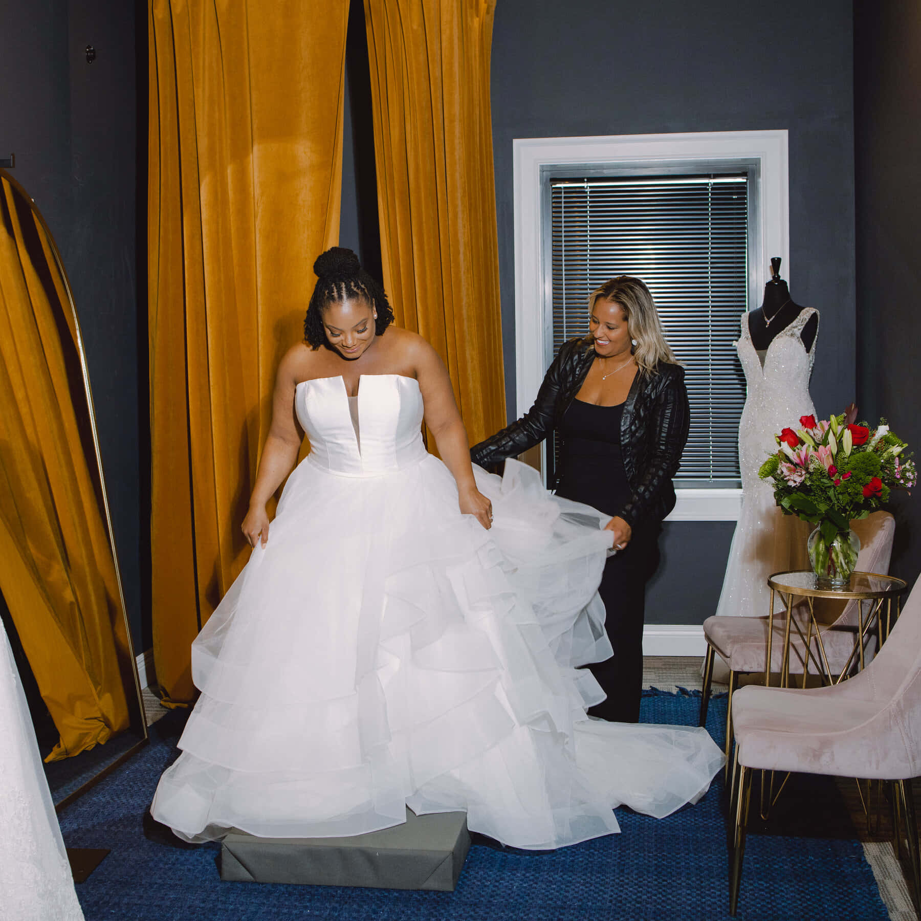 Bride's Dress 桌布 壁紙 — 一位開心的準新娘在時尚精品店裡，在微笑的朋友幫助下試穿一件蓬鬆的白色婚紗。