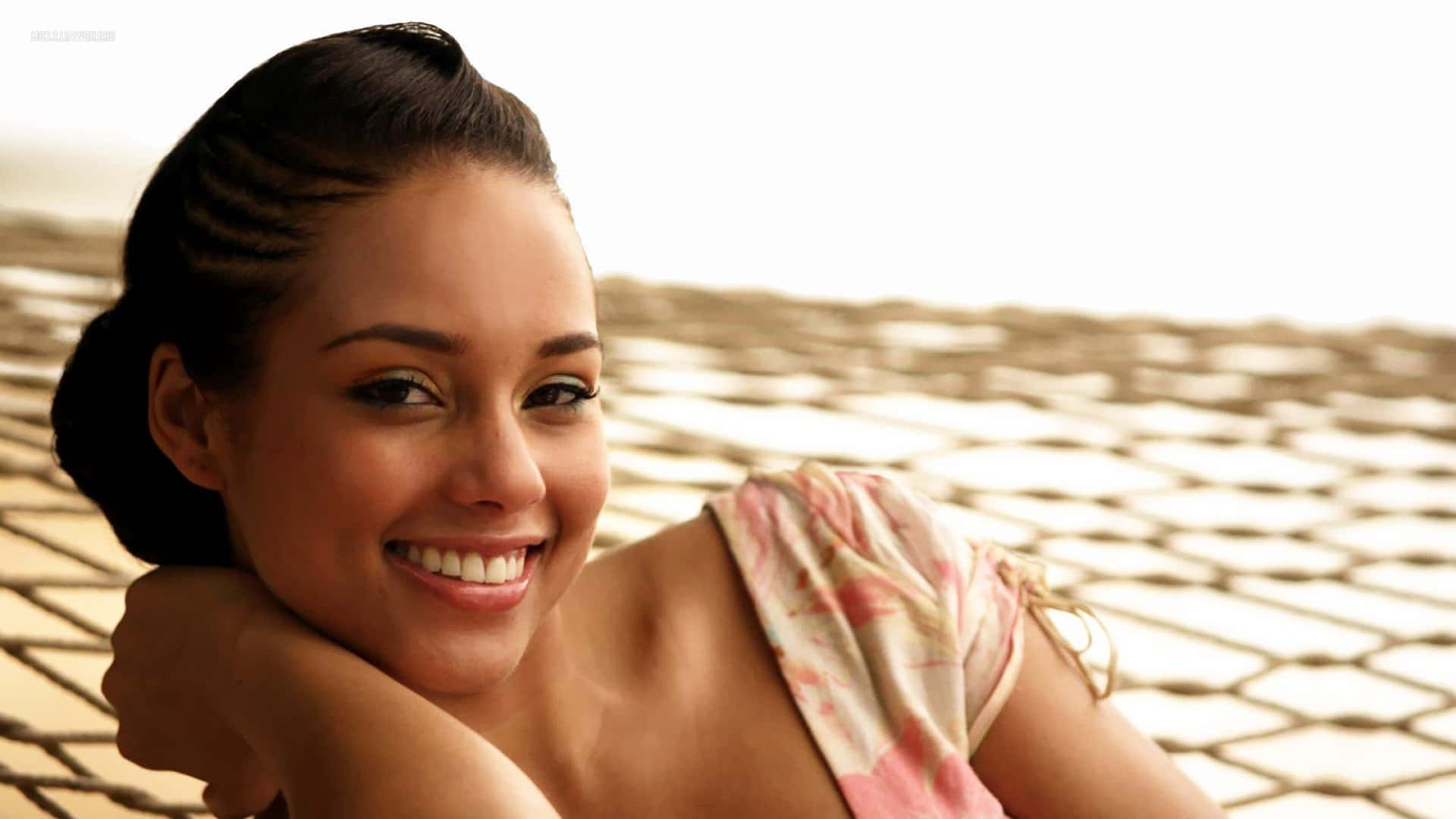 Alicia Keys 桌布 壁紙 — 一位面帶微笑、髮型時尚的女性，在圖案瓷磚背景前將下巴擱在手上。