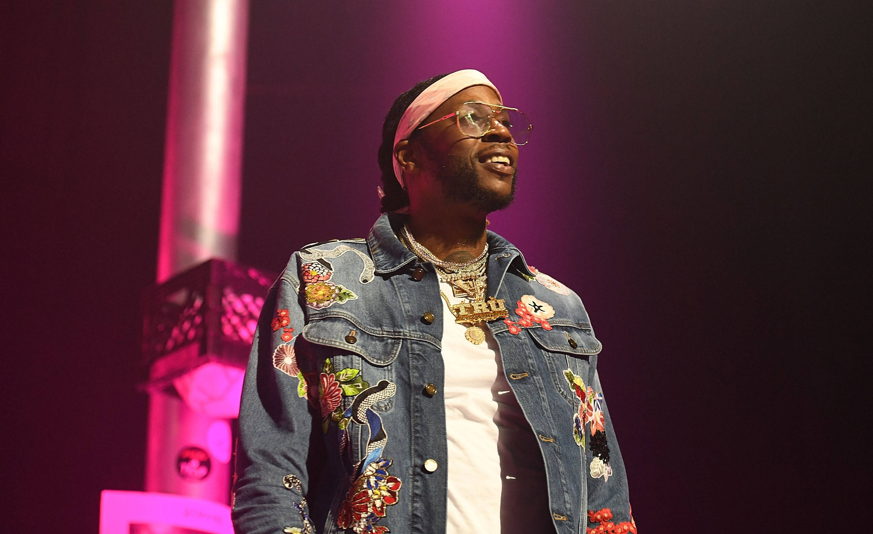 2 Chainz 2017 BET Experience 壁紙 — 一位面帶微笑的男子身穿花卉圖案牛仔外套和眼鏡，在充滿活力的粉紅色舞台燈光下表演。