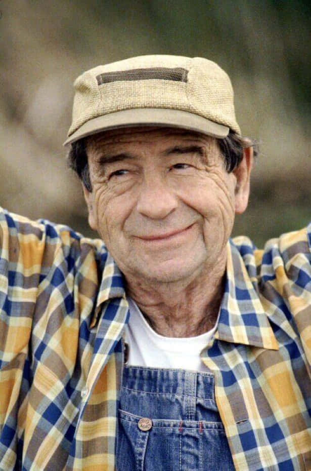 Walter Matthau 桌布 壁紙 — 一位面帶溫暖笑容的長者，在編織帽下穿著格仔襯衫和牛仔工人褲。