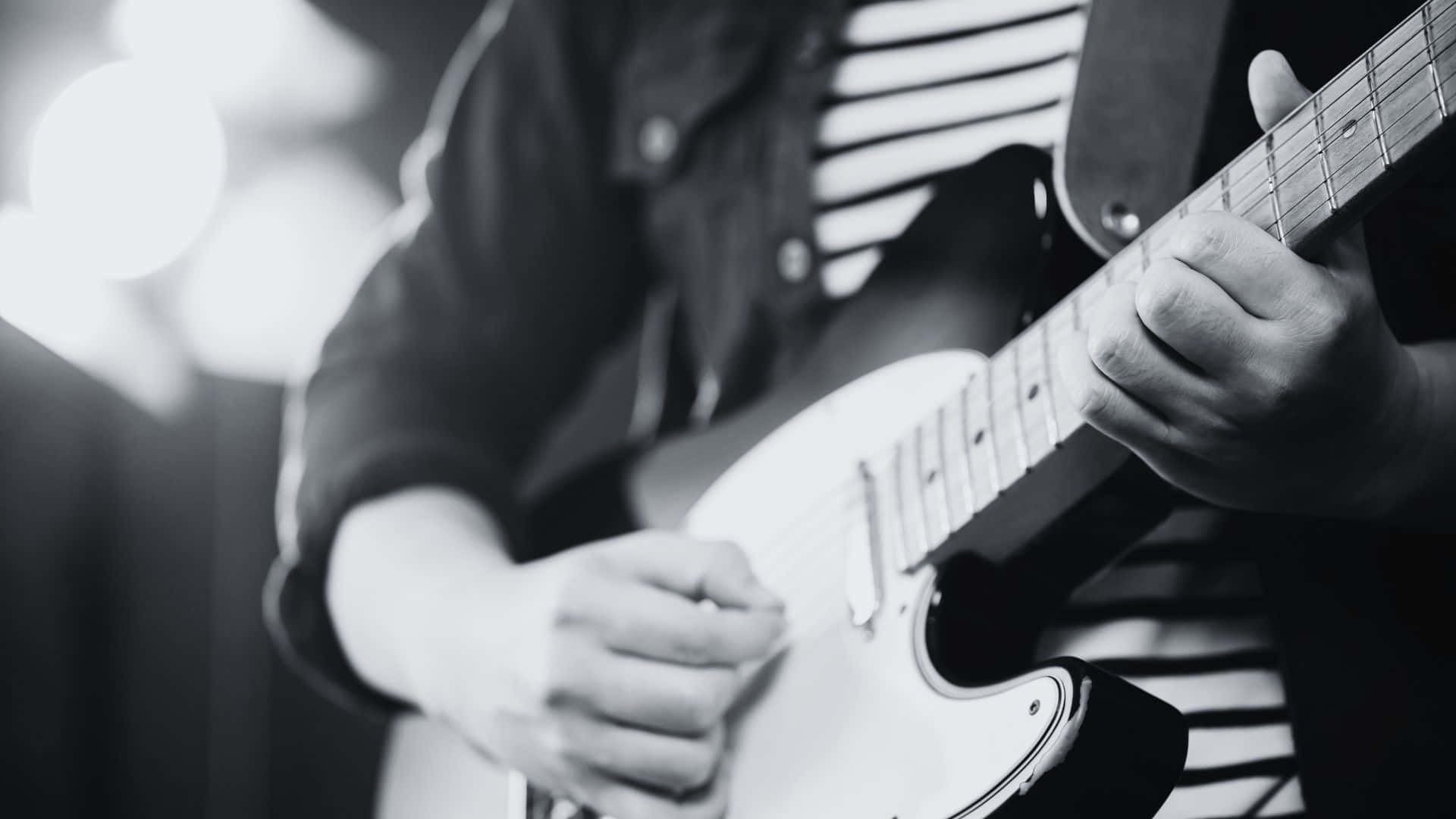 Black And White Guitar 桌布 壁紙 — 一位音樂家的雙手在明亮的舞台燈光下，以黑白風格熟練地彈奏白色電結他。