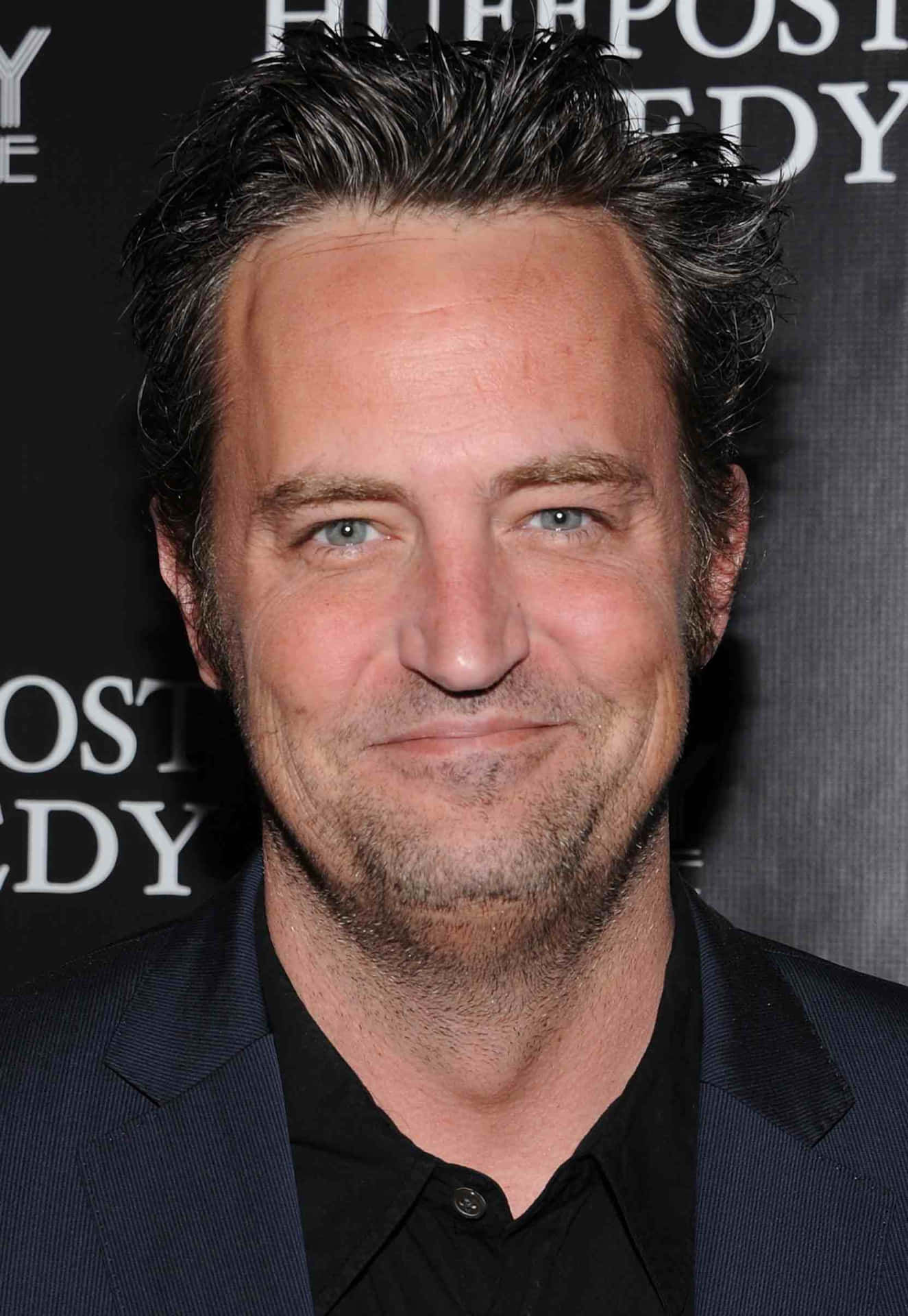 matthew perry 桌布 壁紙 — 一位頭髮花白、帶著微妙微笑的男士的頭像特寫，身穿深色西裝和黑色襯衫。