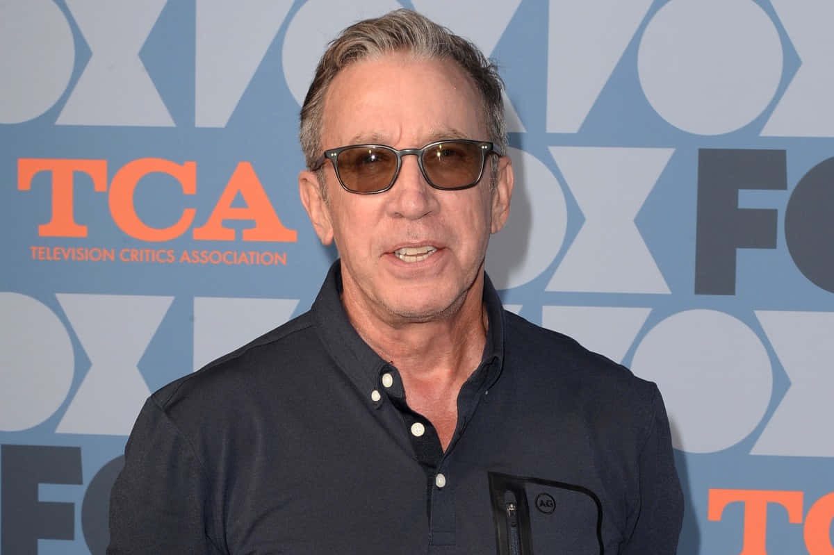 Tim Allen 桌布 壁紙 — 一位頭髮花白、戴著太陽眼鏡的男子在藍色TCA背景板前擺姿勢，背景板上有橙色字樣。