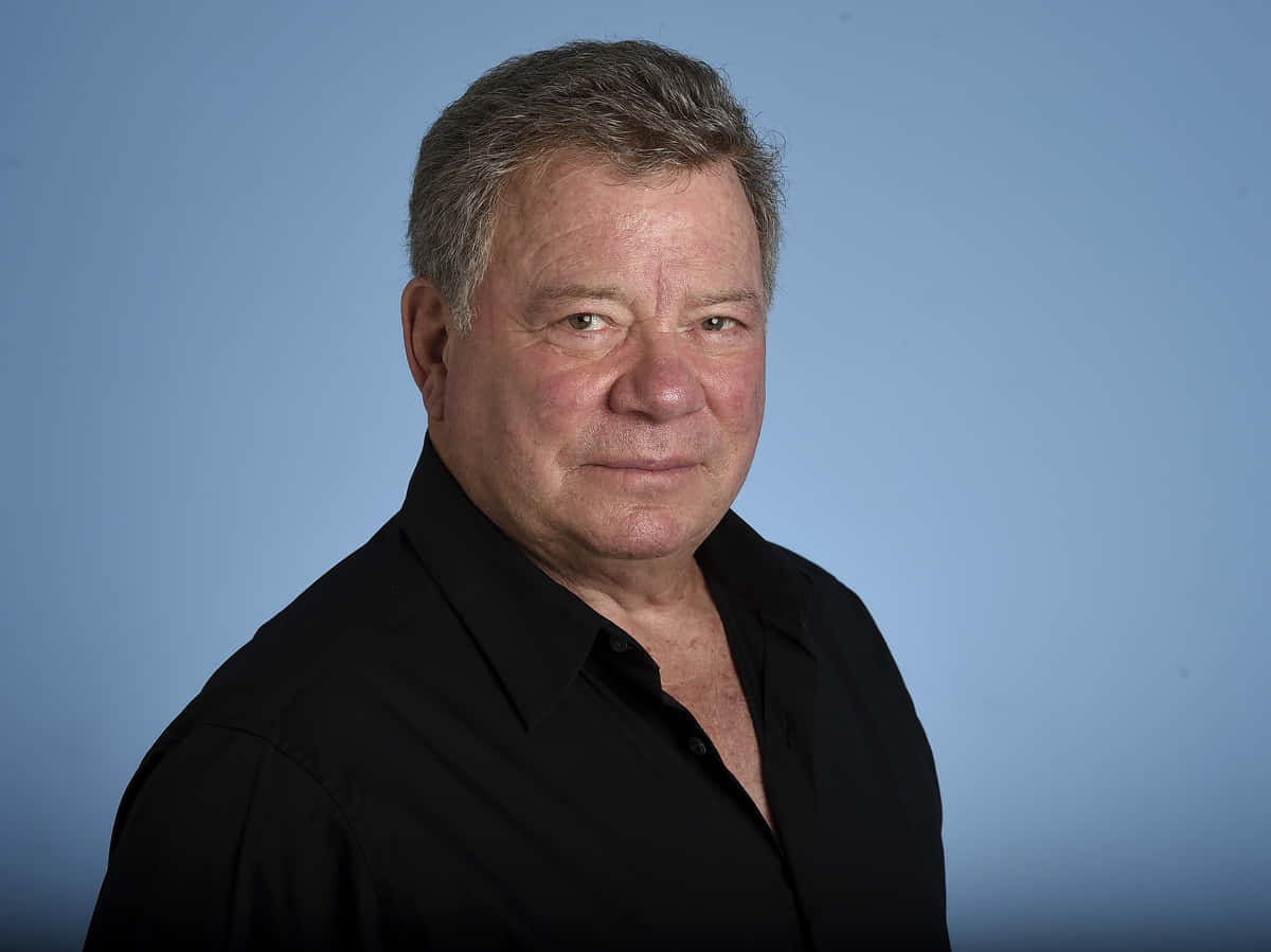 william shatner 桌布 壁紙 — 一位頭髮花白的中年男子穿著黑色襯衫，背景是純藍色攝影棚。