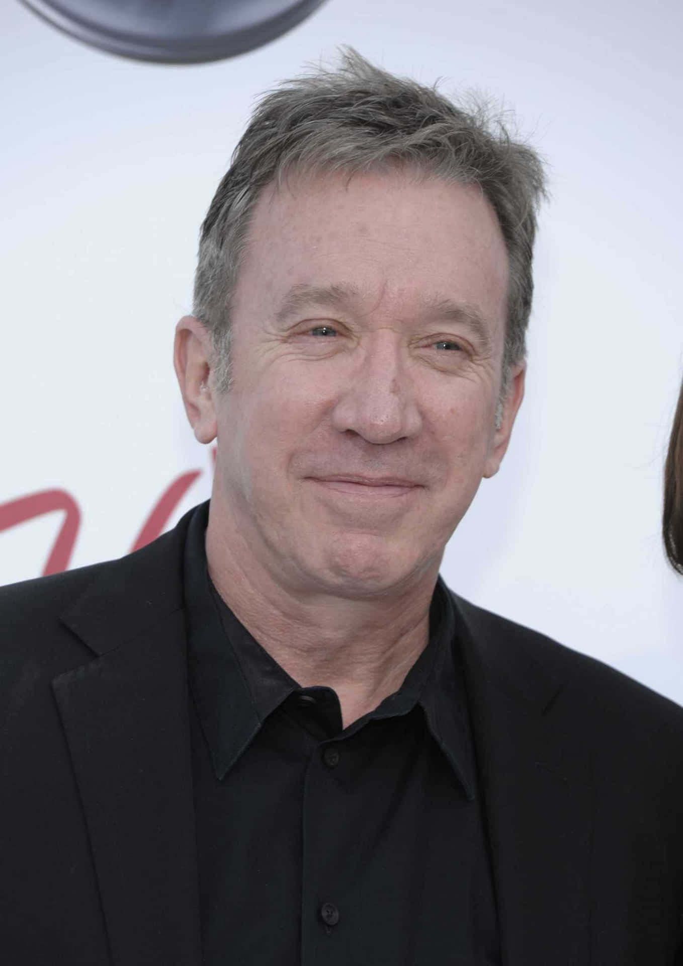 Tim Allen 桌布 壁紙 — 一位頭髮花白的中年男子穿著黑色西裝和襯衫，在明亮的白色背景下的特寫肖像。
