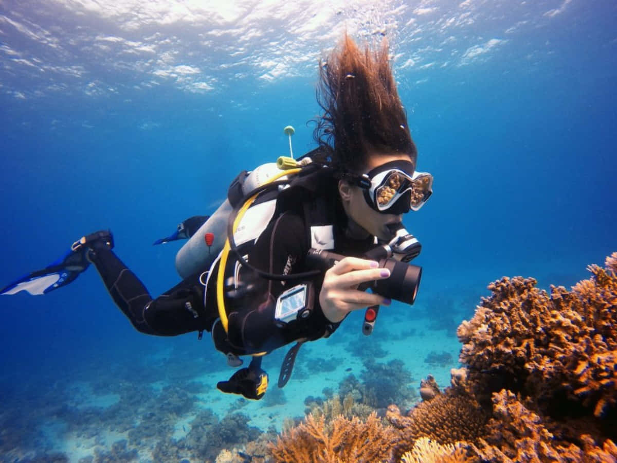 diving 桌布 壁紙 — 一位頭髮飄逸的水肺潛水員在清澈的藍色海洋中拍攝珊瑚礁照片。