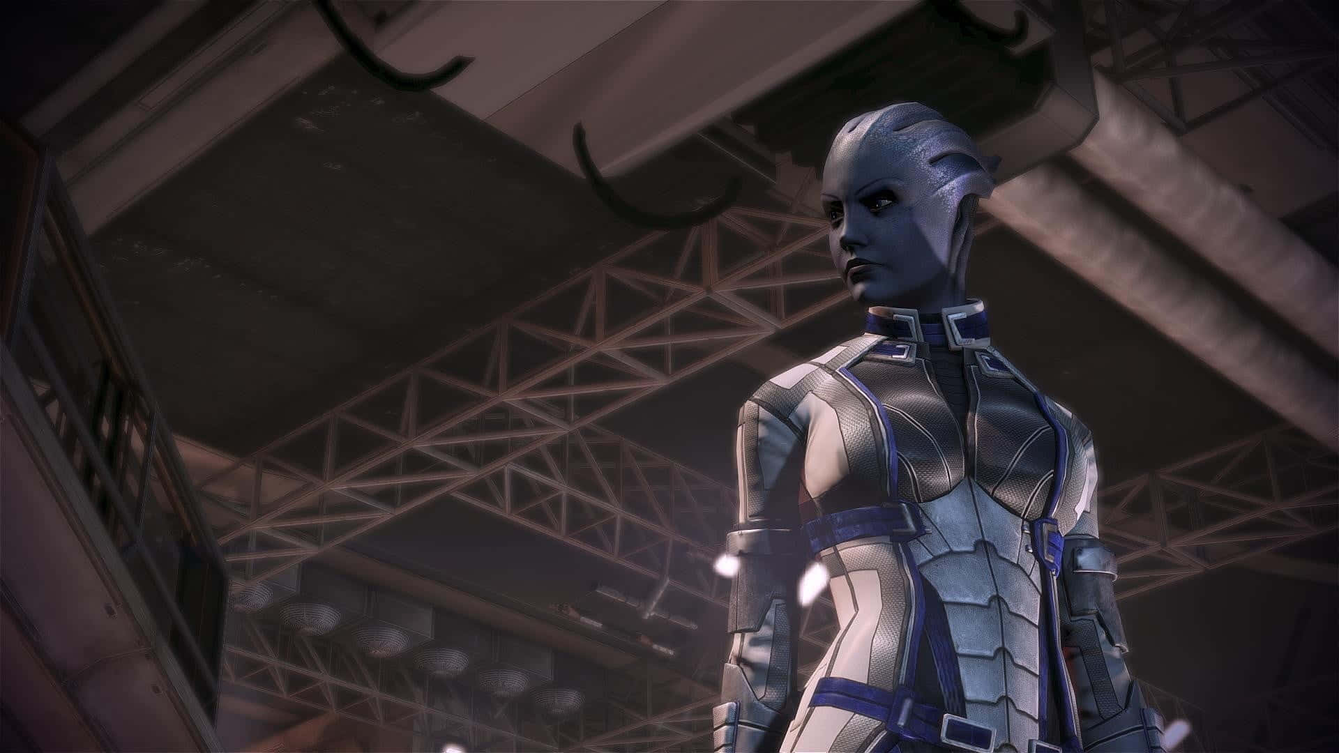 Liara T'soni 桌布 壁紙 — 一位高大的外星女性穿著銀色和藍色裝甲服，莊嚴地站在昏暗機庫的工業鋼樑下。