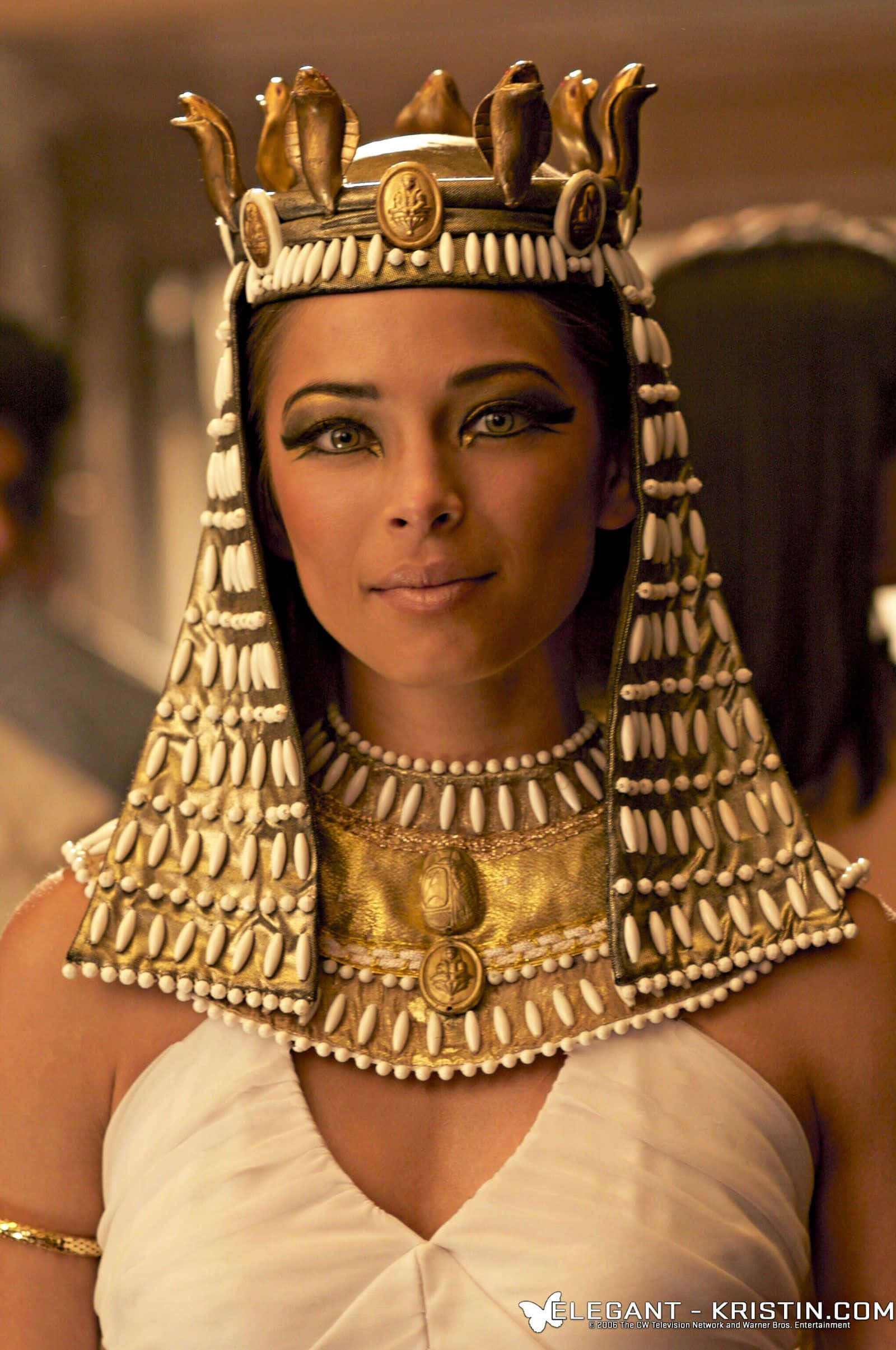 Cleopatra 桌布 壁紙 — 一位高貴的女性，戴著華麗的金色埃及頭飾和項圈，在溫暖的燈光下以銳利的眼神向前凝視。