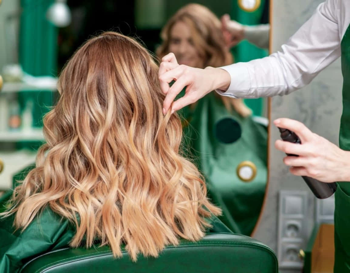 Hair Salon 桌布 壁紙 — 一位髮型師在綠色沙龍椅上為客戶噴霧並造型波浪金髮，鏡中有倒影。