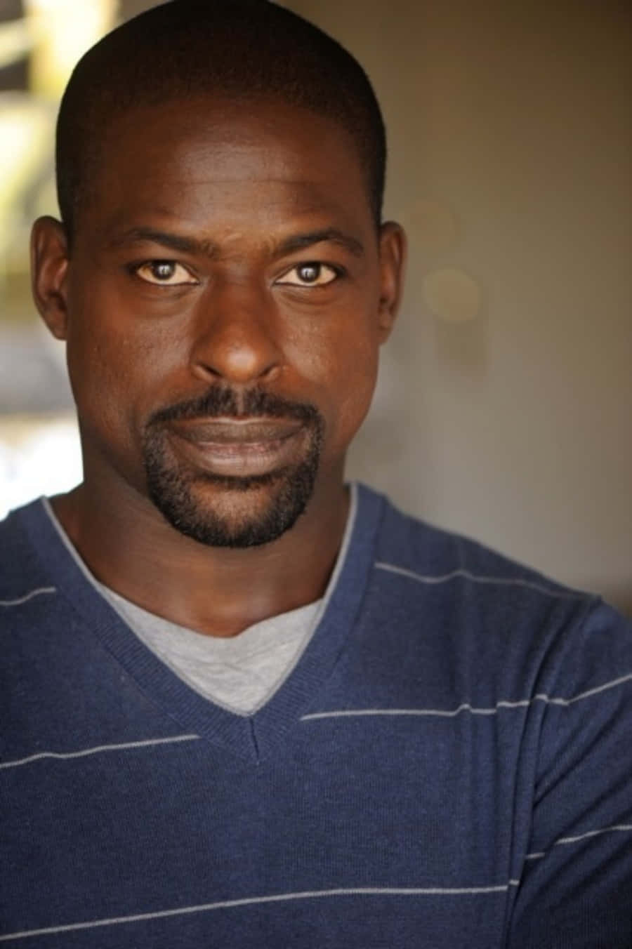 Sterling K Brown 桌布 壁紙 — 一位鬍子修剪整齊的黑人男子近距離肖像，身穿灰色T恤外搭藍色條紋毛衣。