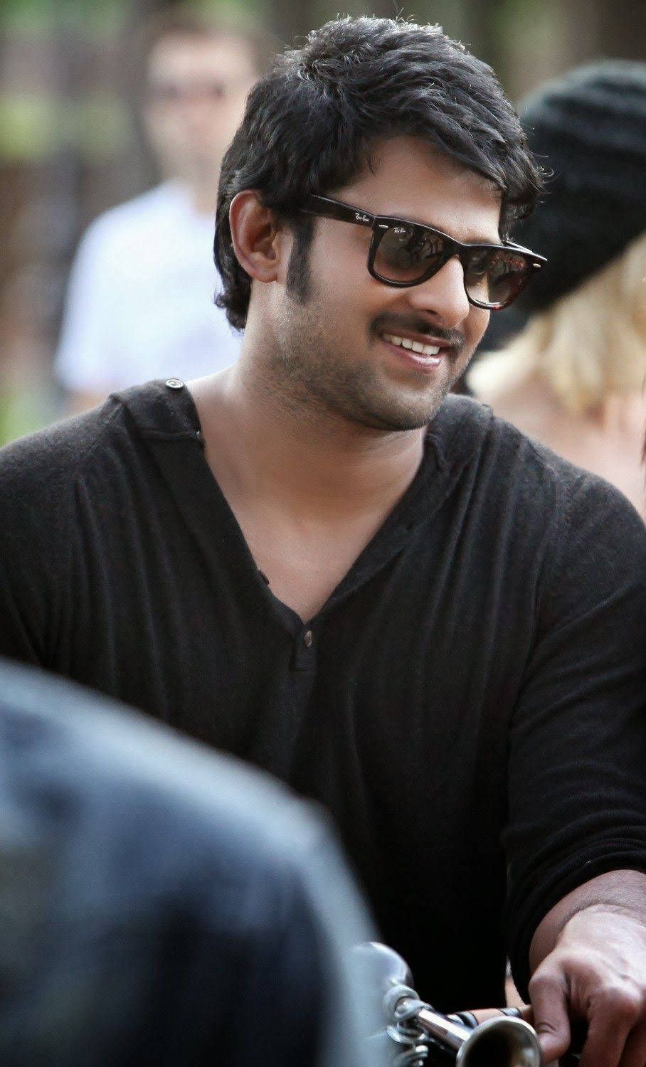 Prabhas Mirchi 桌布 壁紙 — 一位黑髮、戴太陽眼鏡的男士微笑著騎電單車穿過模糊的戶外場景。
