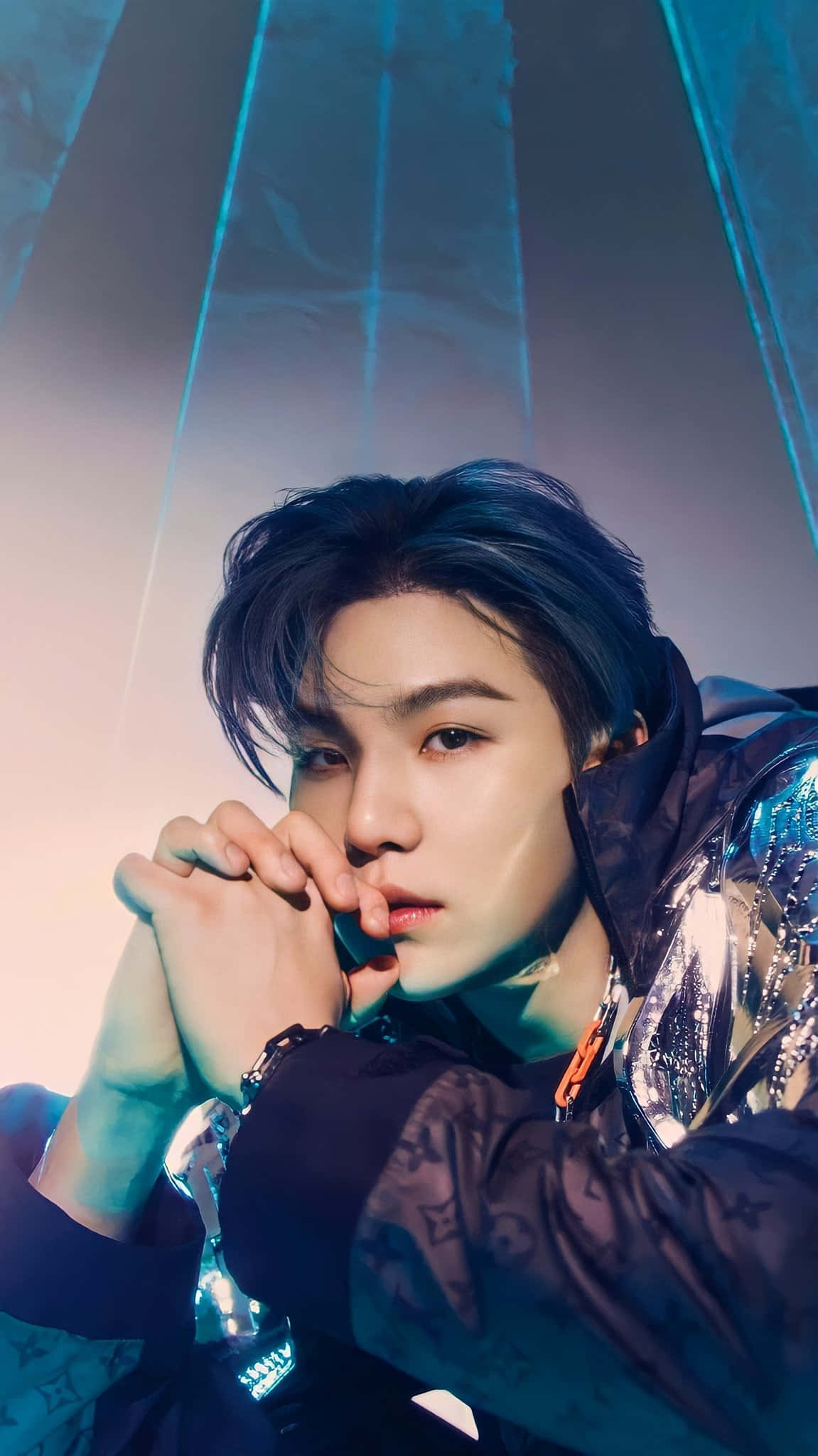Suga 桌布 壁紙 — 一位黑髮、眼神銳利的年輕男子，在戲劇性的藍色和粉紅色燈光下穿著閃亮外套。