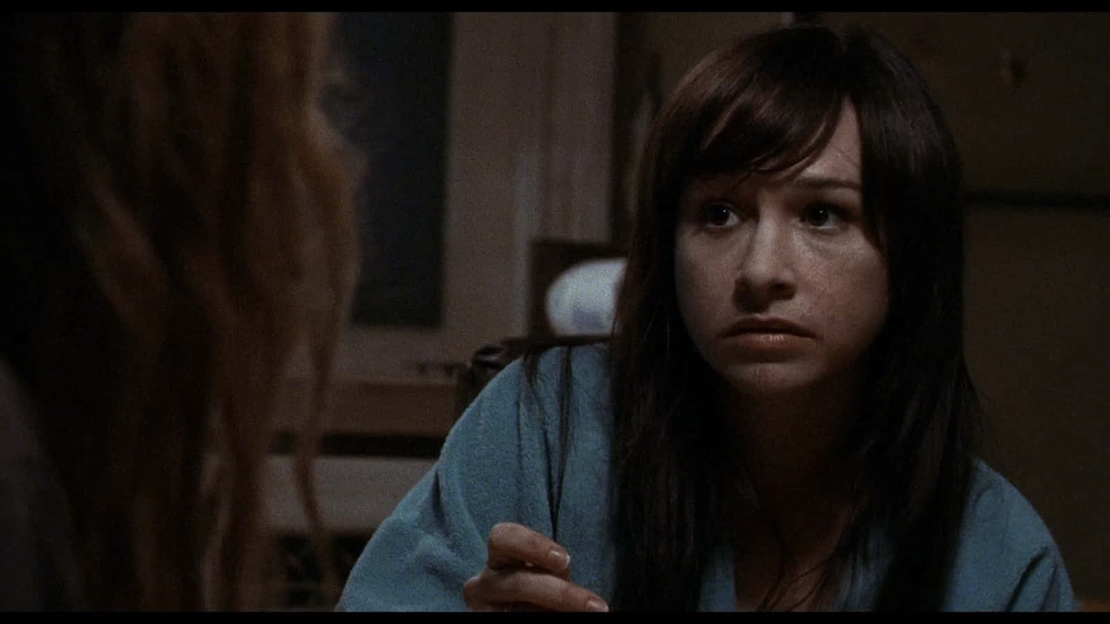 Danielle Harris 桌布 壁紙 — 一位黑髮、身穿藍色長袍的女子在昏暗的房間裏專注地凝視着另一個人。