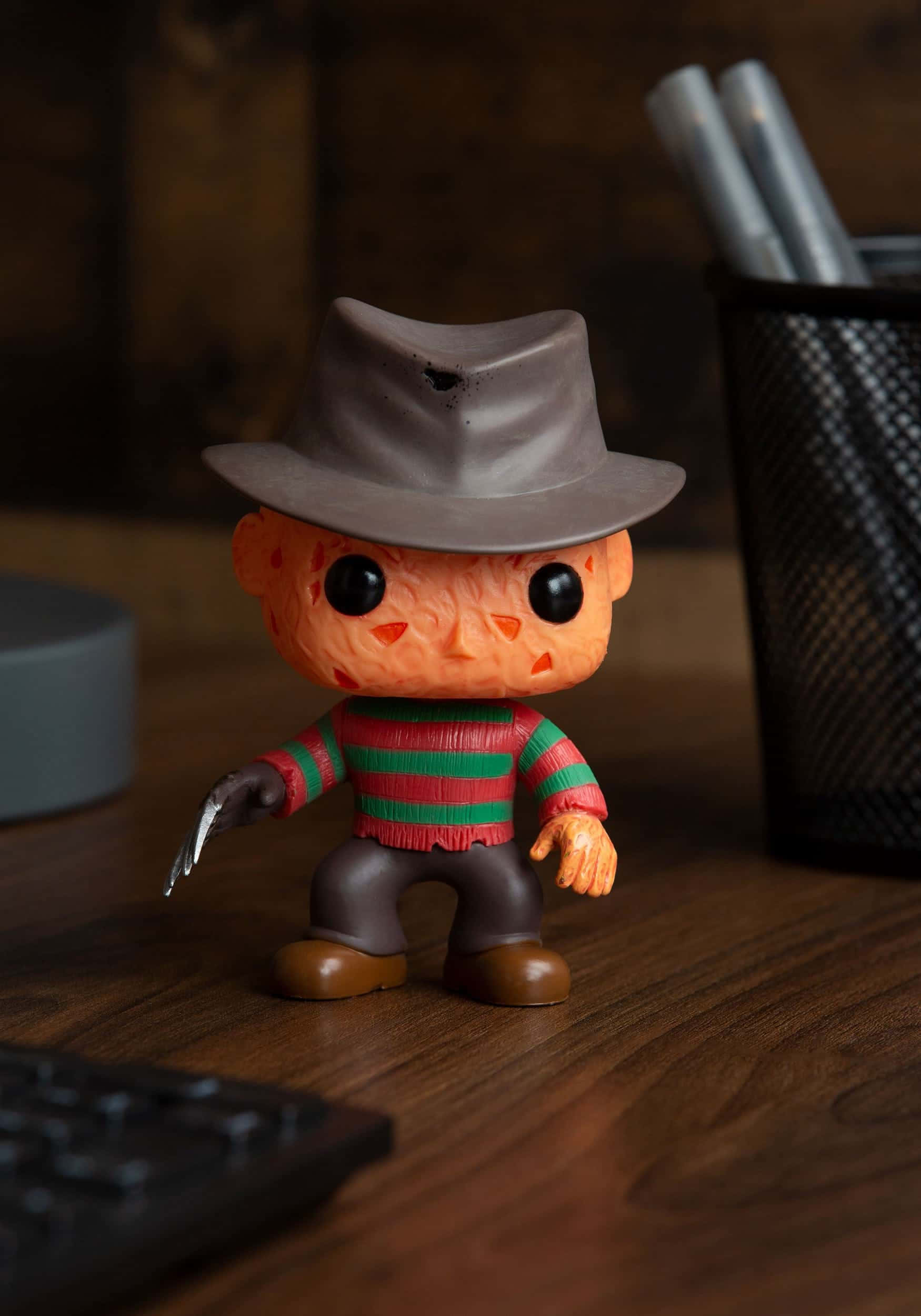 費迪·克魯格 桌布 壁紙 — 一個 Freddy Krueger Funko Pop! 人偶站在木桌上，旁邊有鍵盤和筆筒。