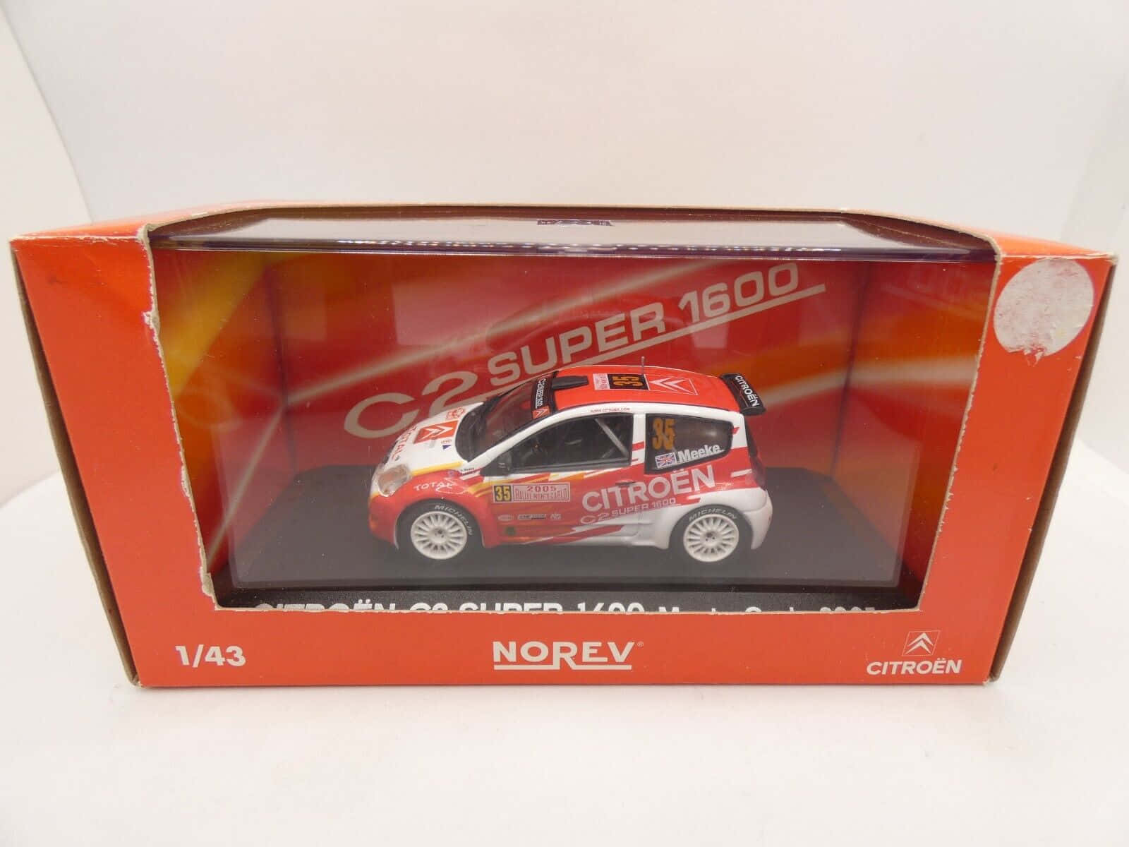  壁紙 — 一個1:43比例的雪鐵龍C2 Super 1600拉力賽車模型，採用紅白黑配色，展示在其橙色品牌盒中。