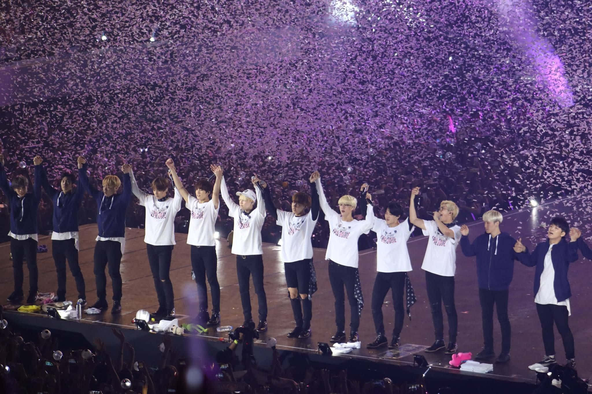 Bts Stage 桌布 壁紙 — 一個K-pop組合在明亮的燈光下於演唱會中慶祝，紫色紙屑如雨般落下。