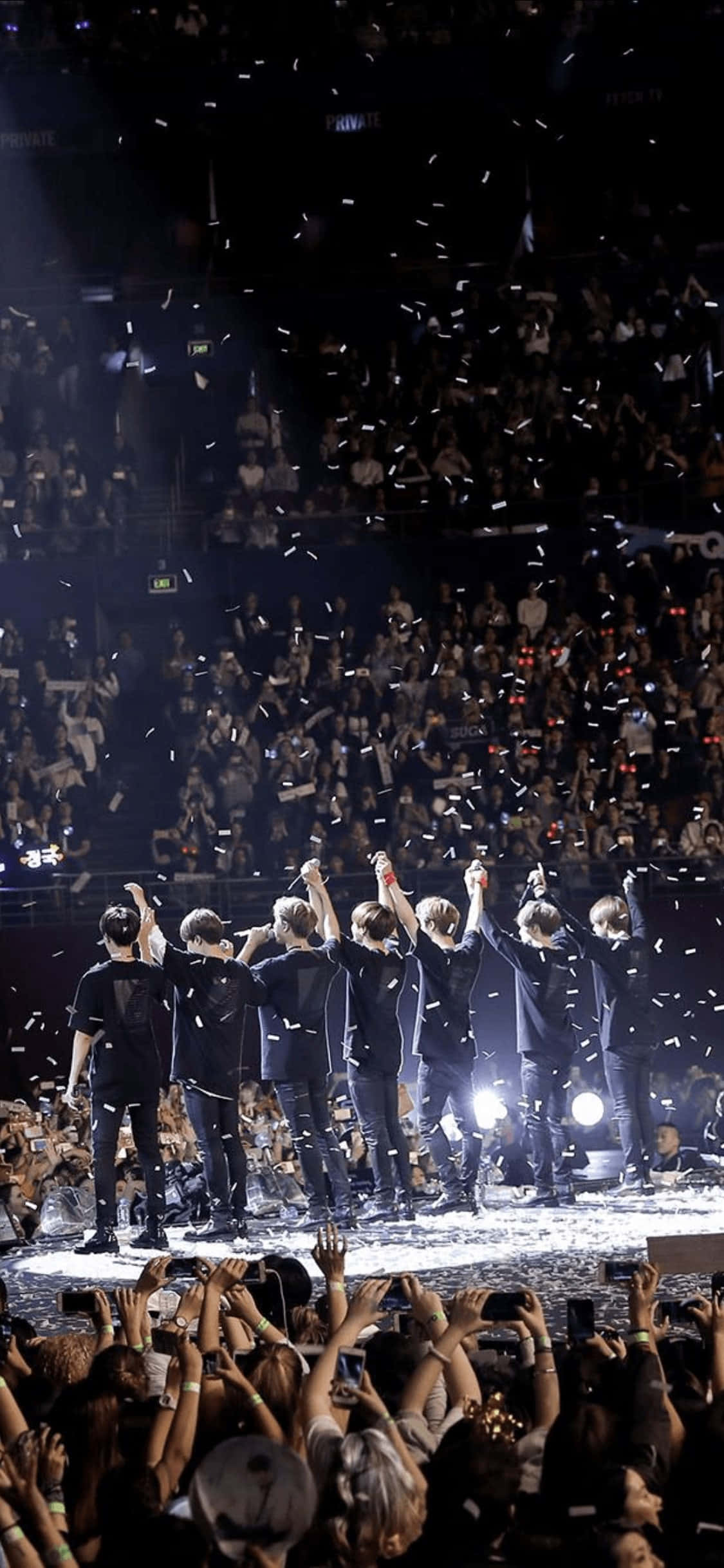 Bts Stage 桌布 壁紙 — 一個K-pop組合在明亮的燈光下於舞台上慶祝，五彩紙屑如雨般灑落在下方狂歡的人群中。