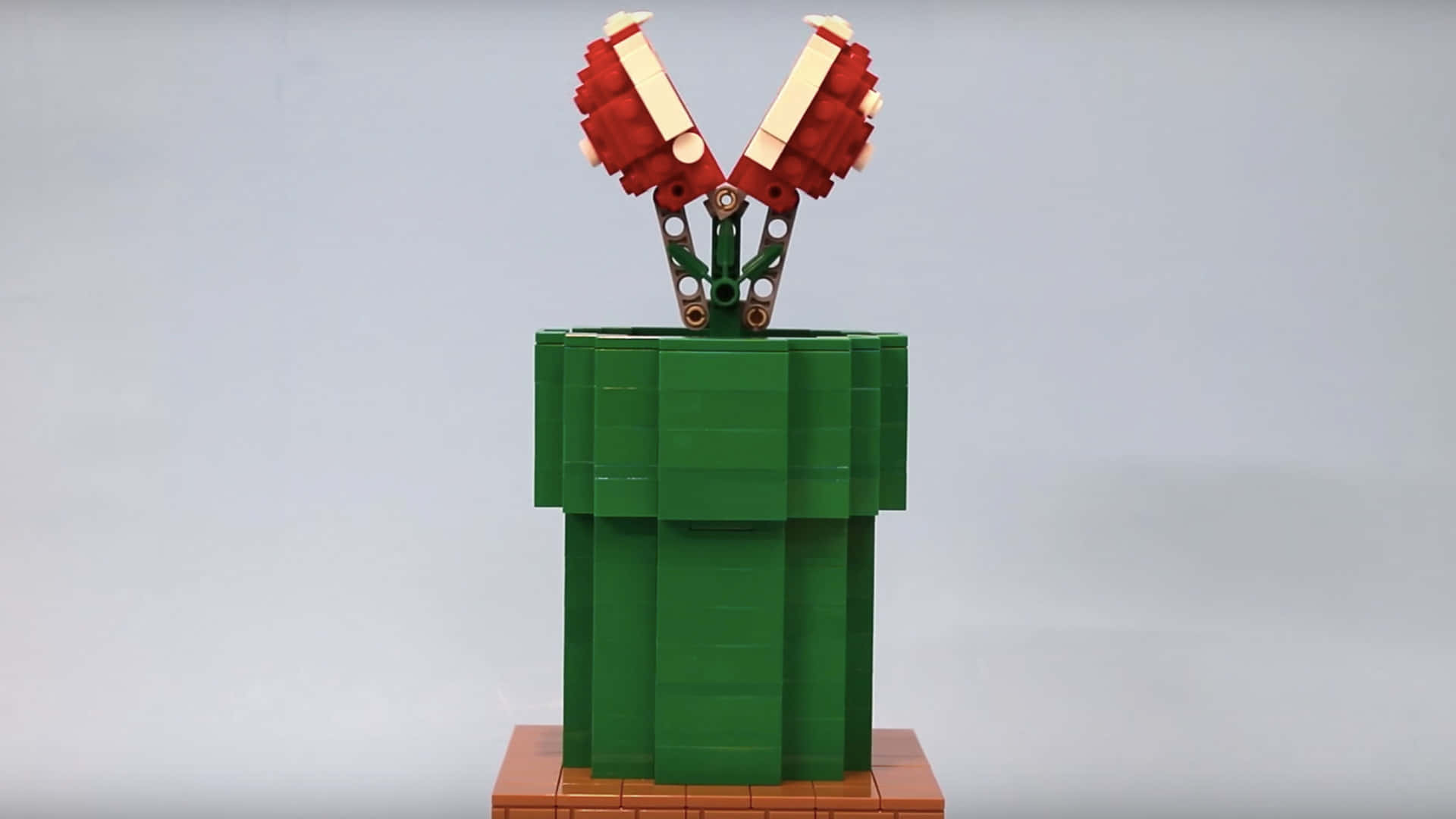 piranha plant 桌布 壁紙 — 一個LEGO模型，展示超級瑪利歐的綠色管道，頂部冒出紅色和白色的蘑菇帽，背景為純灰色。