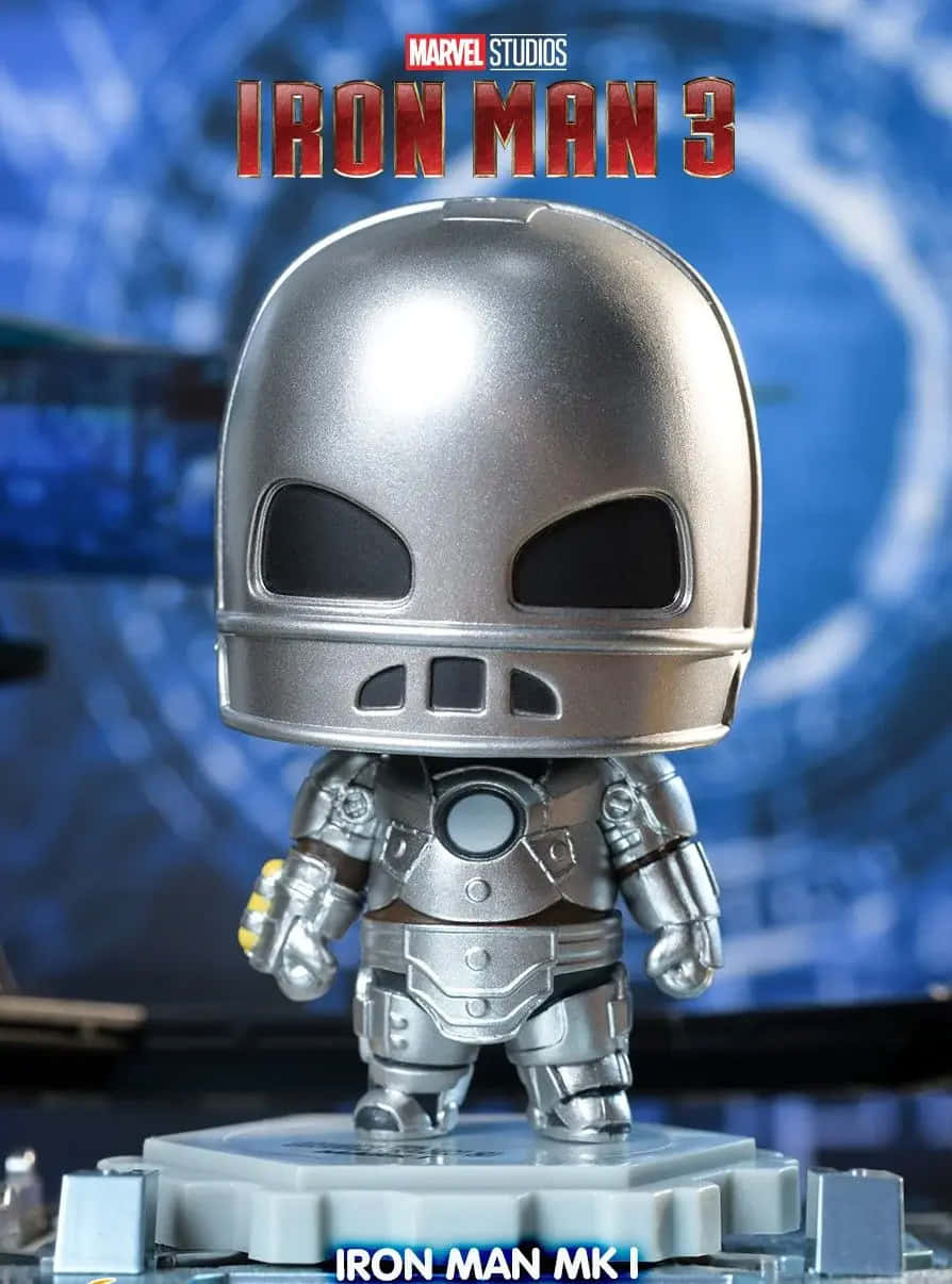 Iron Man Bobbleheads 桌布 壁紙 — 一個Q版風格的鐵甲奇俠MK I動作人偶站在灰色底座上，背景是帶有電影標題文字的藍色模糊背景。