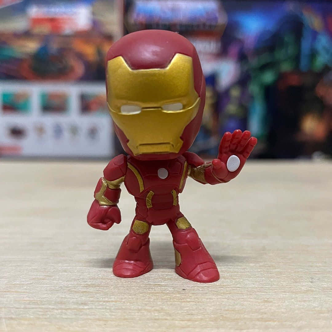 Iron Man Bobbleheads 桌布 壁紙 — 一個Q版風格的鐵甲奇俠動作人偶站在木質表面上，背景是模糊的漫畫書。