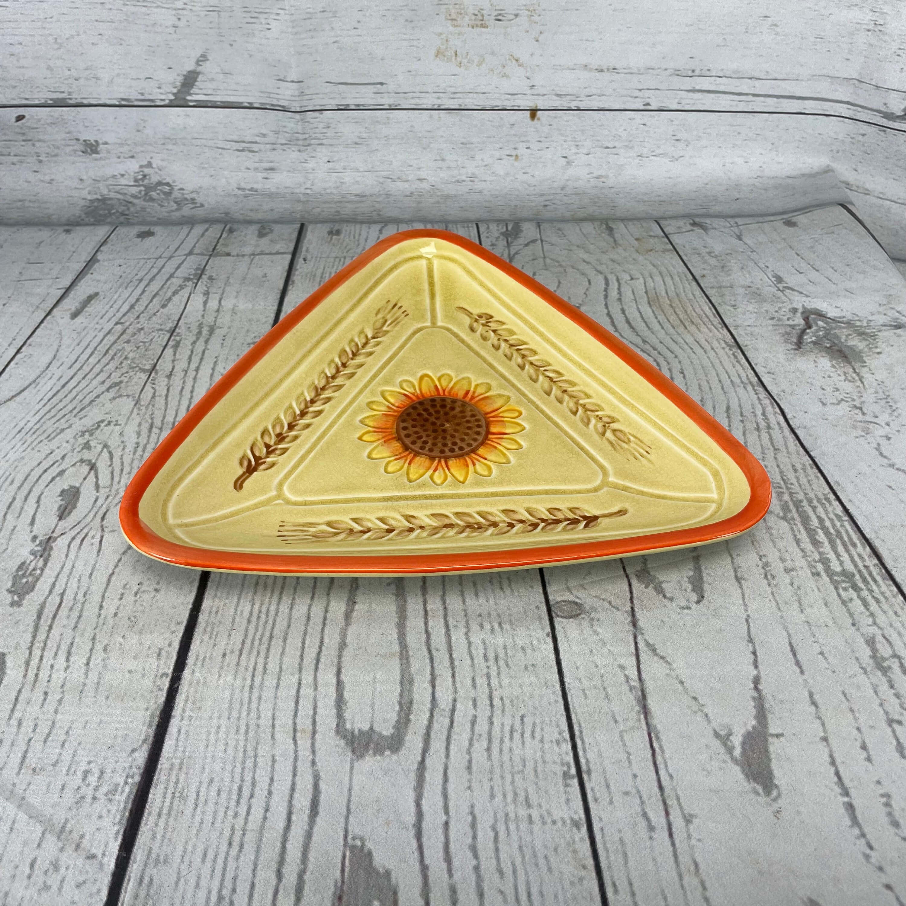 Yellow Triangle 桌布 壁紙 — 一個三角形陶瓷碟，帶有向日葵和小麥圖案，放在風化的白色木板上。