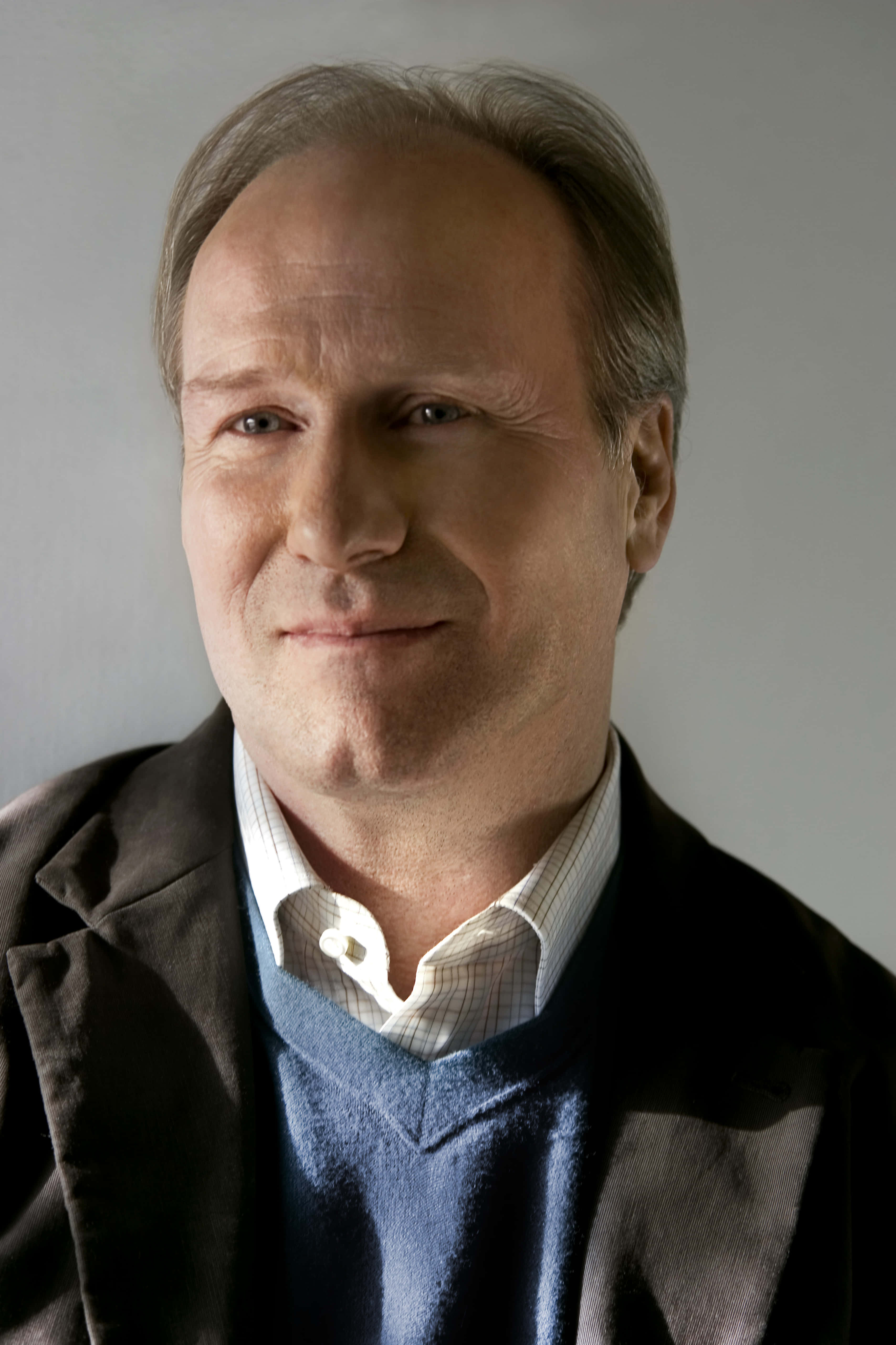 William Hurt 桌布 壁紙 — 一個中年男人嘅特寫肖像，佢有灰白頭髮，著住藍色冷衫同啡色外套，背景係純灰色。
