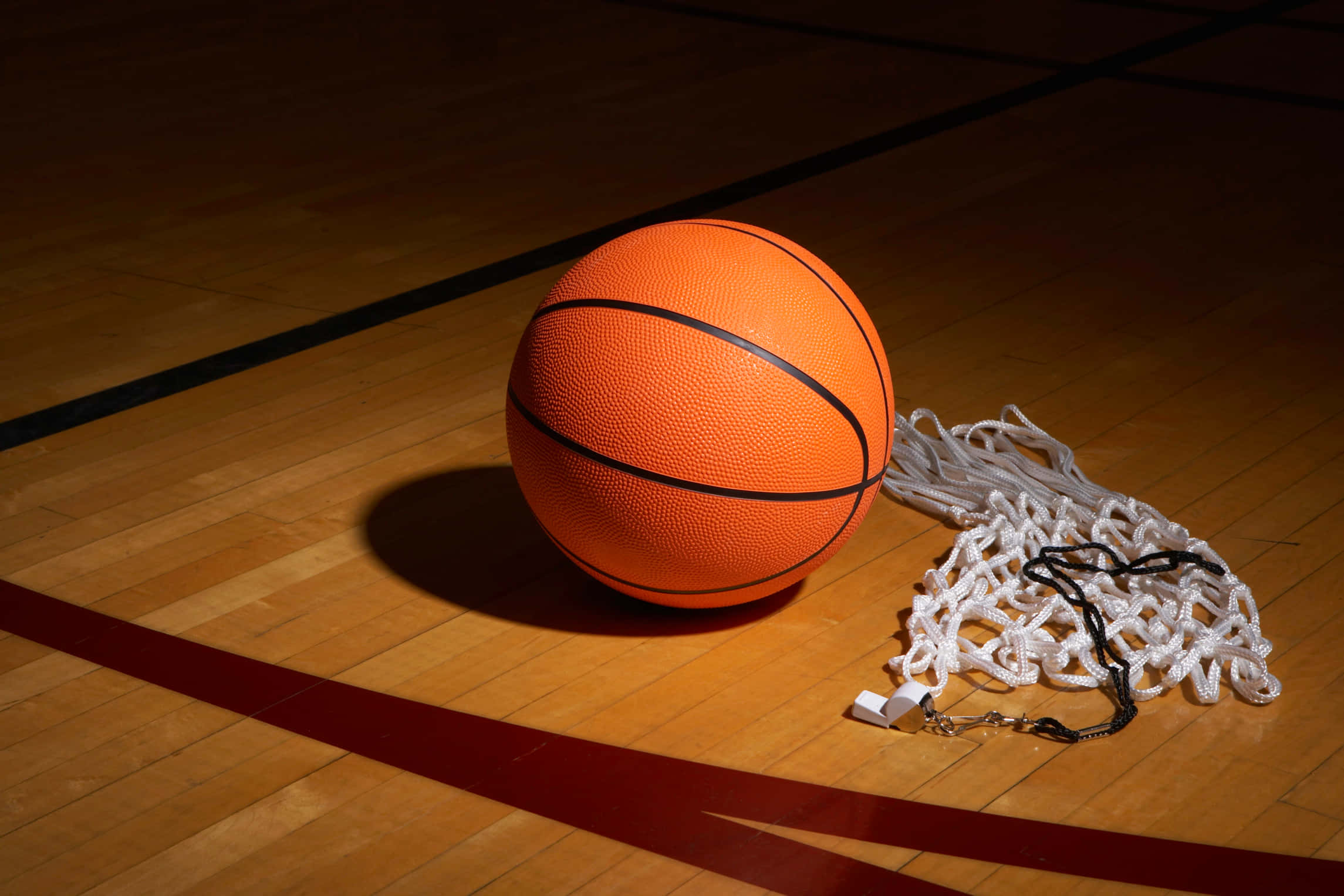 Cool Basketball 桌布 壁紙 — 一個亮橙色的籃球放在拋光木地板上，旁邊有一個皺巴巴的白色網，在戲劇性的聚光燈下。