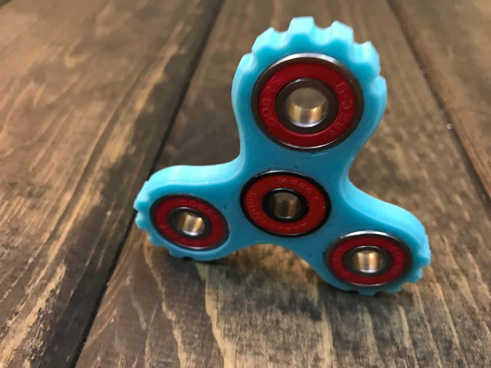 Fidget 桌布 壁紙 — 一個亮藍色的指尖陀螺帶有紅色軸承，放置在經風化的木質表面上。