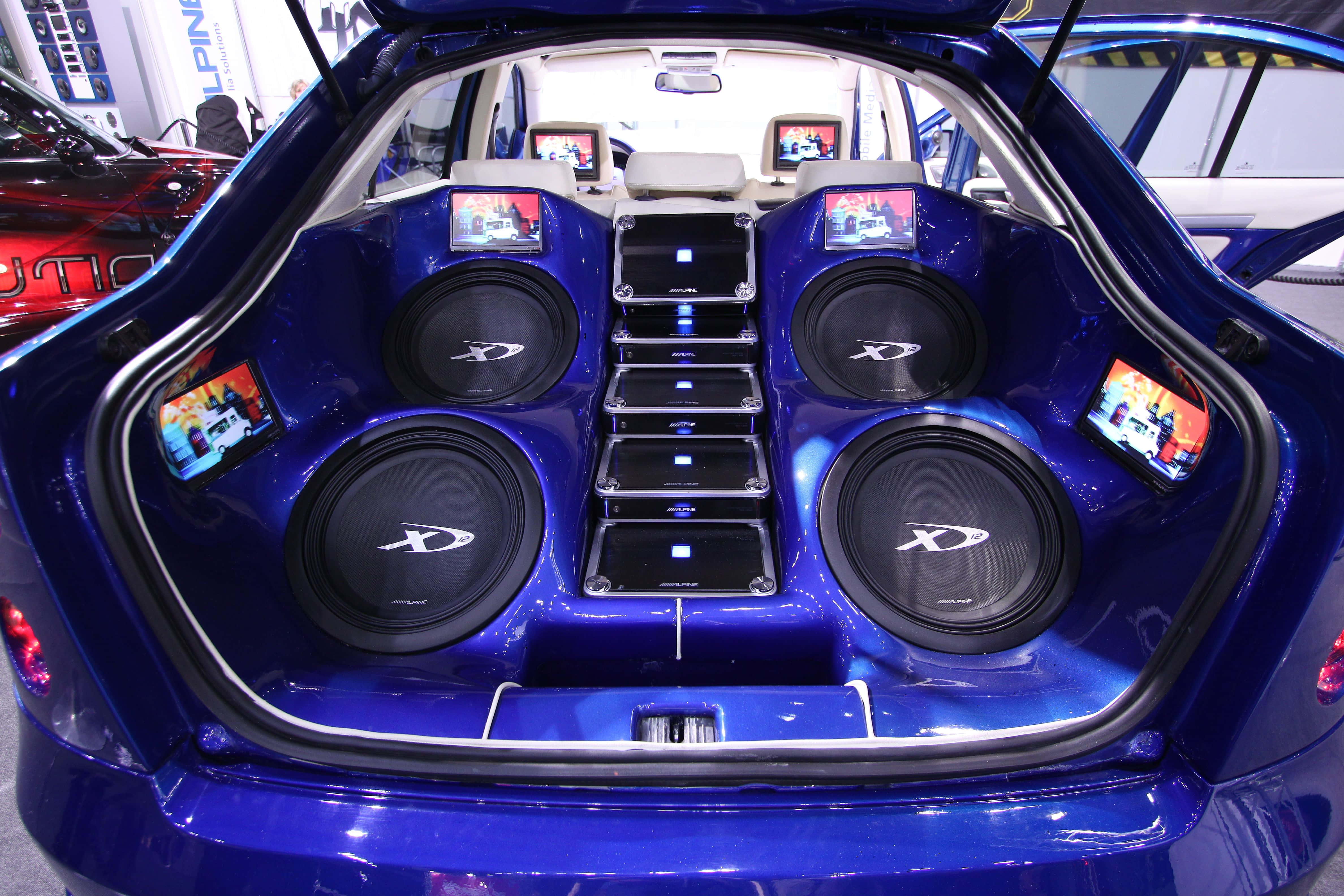 Car Audio 桌布 壁紙 — 一個亮面藍色汽車尾箱，改裝了四個大型超低音揚聲器和多個小型屏幕，顯示汽車音響內容。