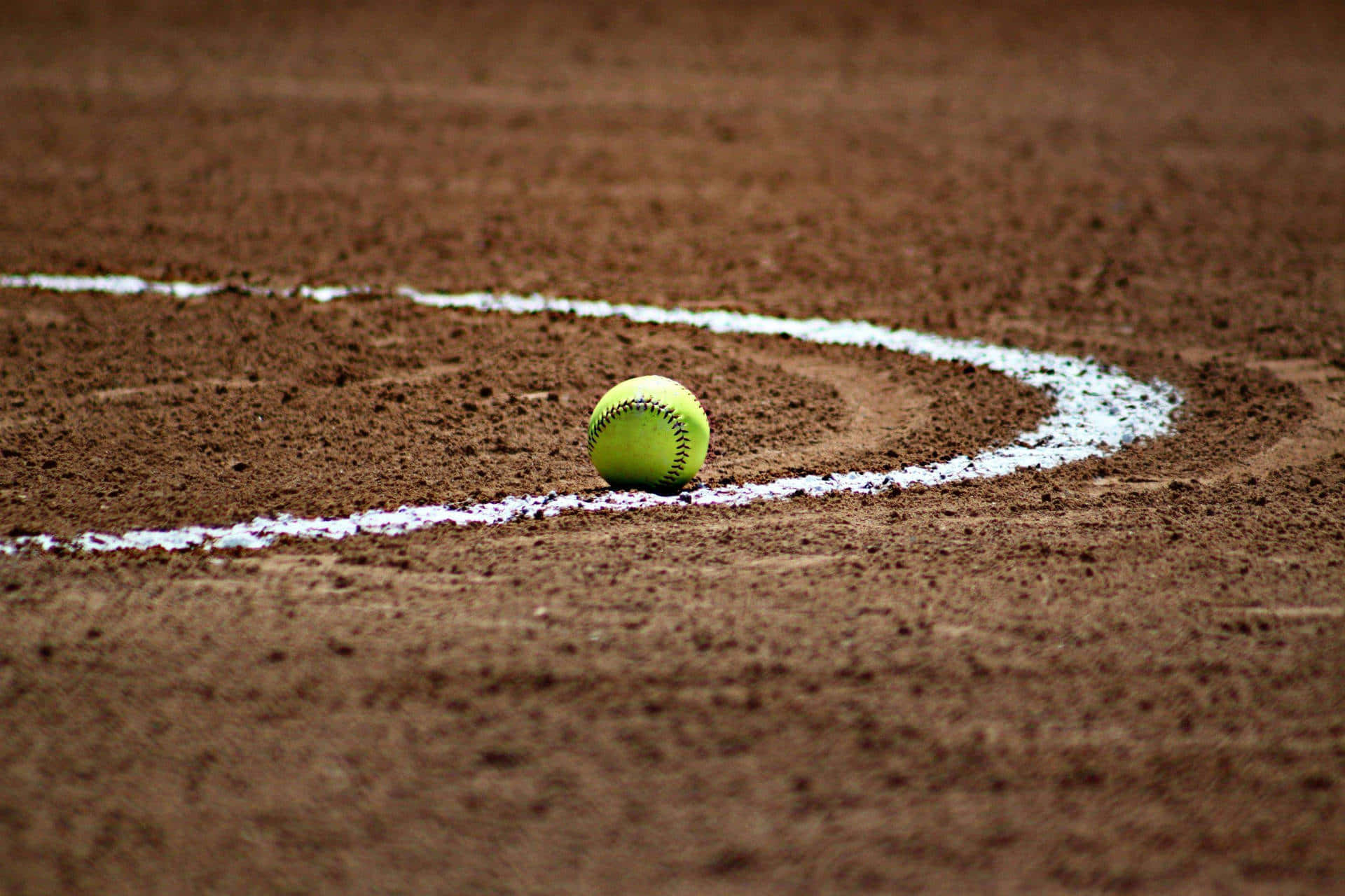 Softball 桌布 壁紙 — 一個亮黃色的壘球放在棕色泥土場地上刻劃的彎曲白色粉筆線上。