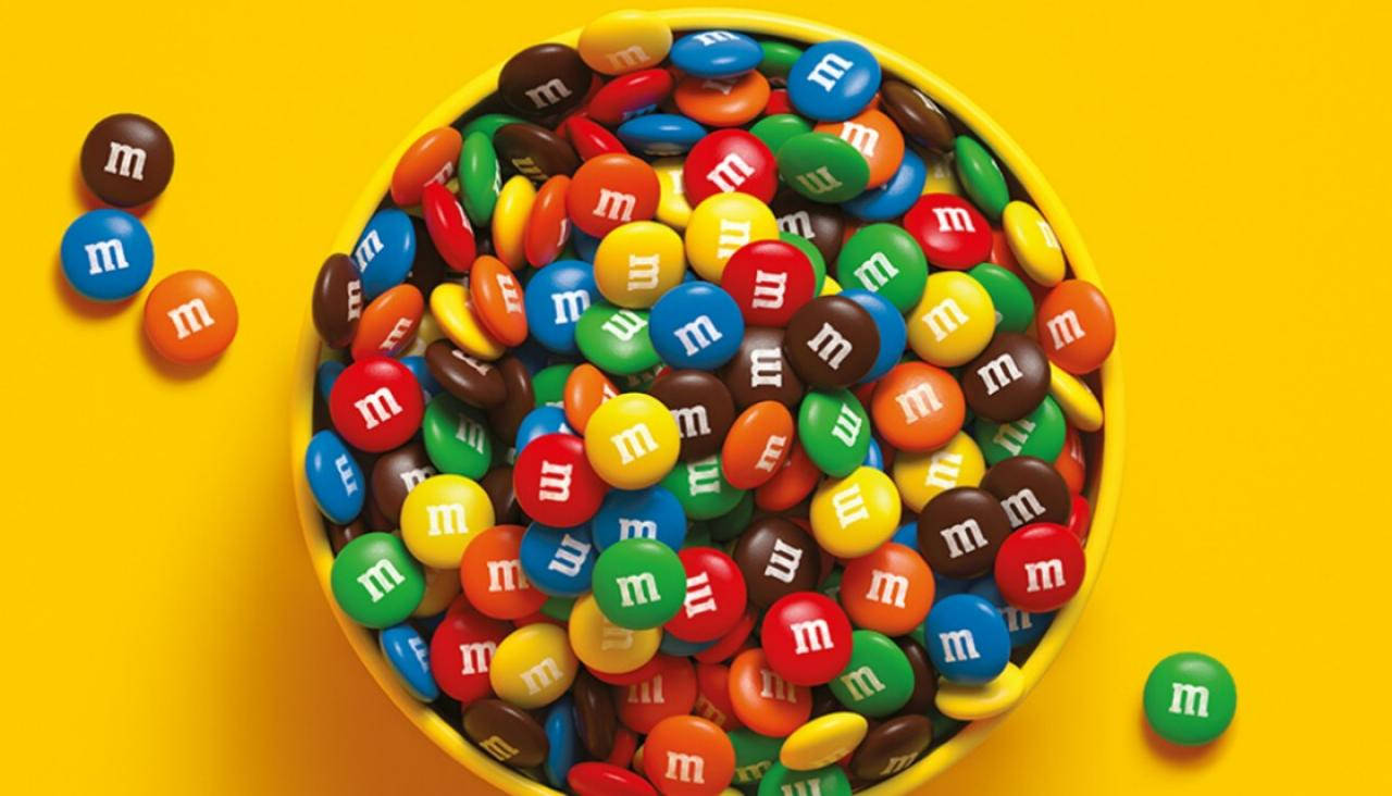 Chocolate 桌布 壁紙 — 一個亮黃色的碗，裝滿了色彩繽紛的M&M's糖果，襯托著充滿活力的黃色背景。