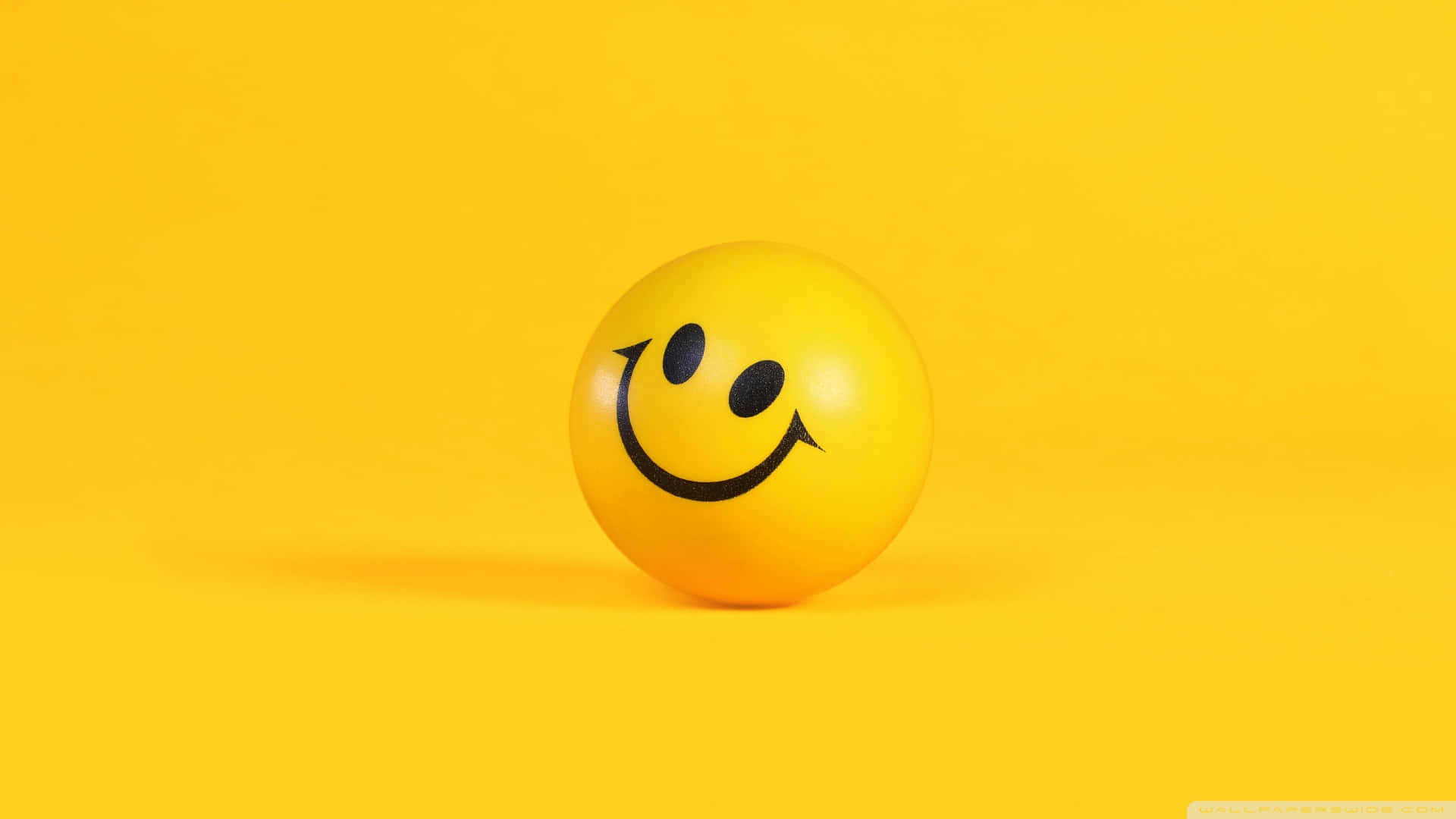 Smiley 桌布 壁紙 — 一個亮黃色的笑臉波波球放在純黃色背景上，投射出柔和的陰影。