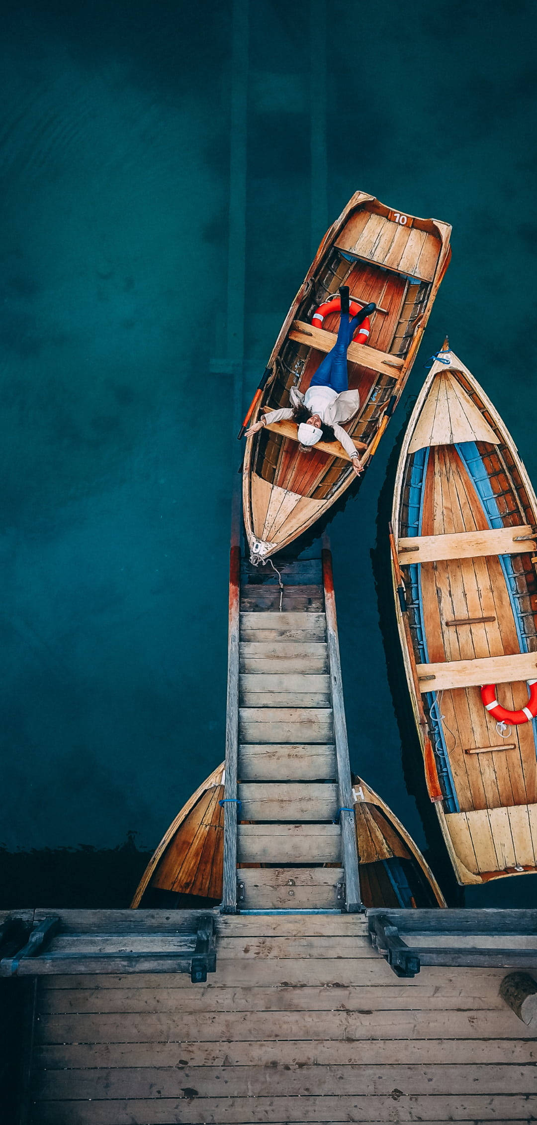 Boat 桌布 壁紙 — 一個人倒臥在一艘停泊在碼頭的木船上，周圍是深藍綠色的海水。